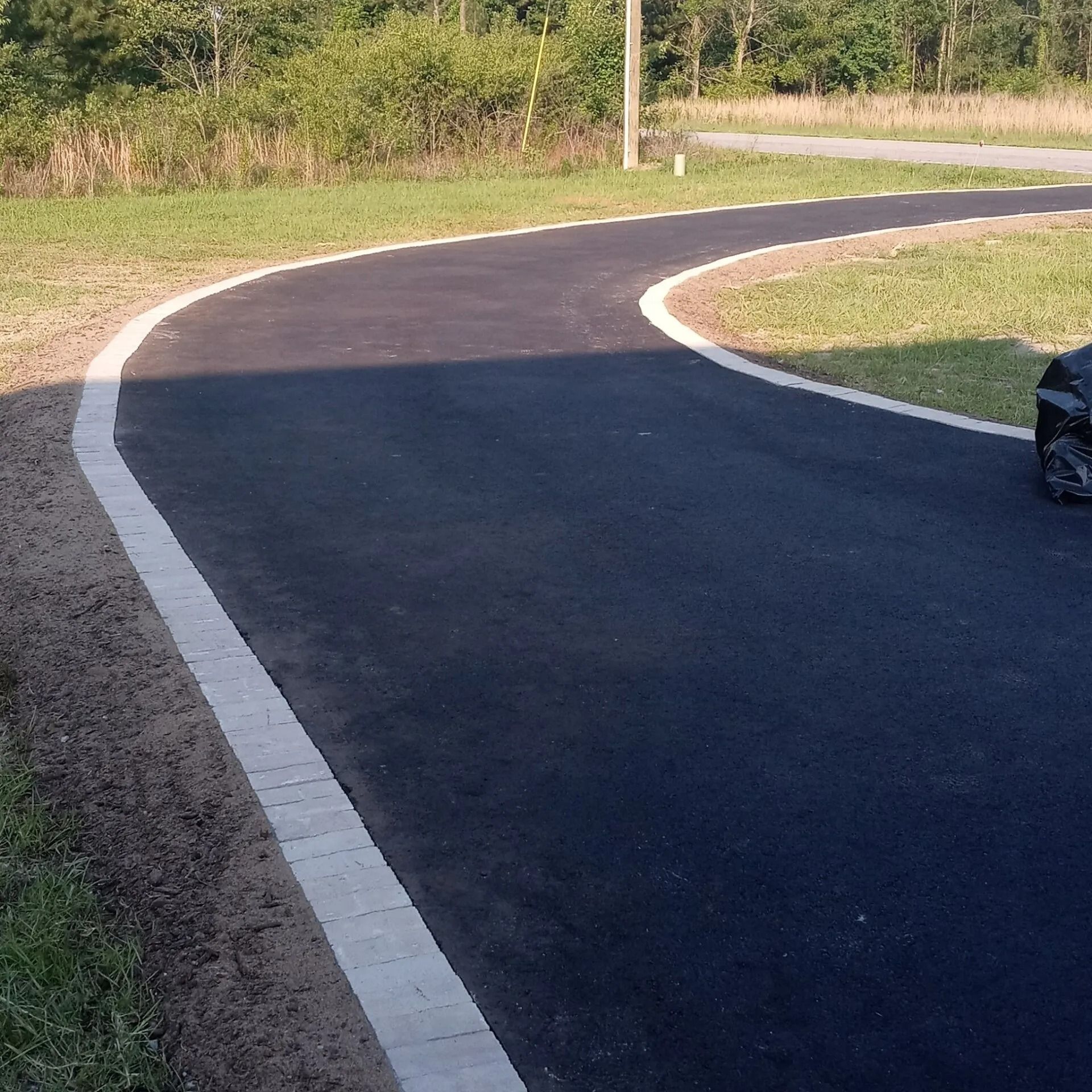 Curved black asphalt path with white edges beside grass and trees in daylight