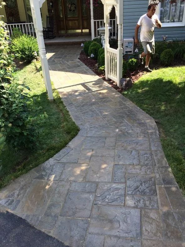 Stone walkway curving through a garden toward a house entrance, with a person near the doorway