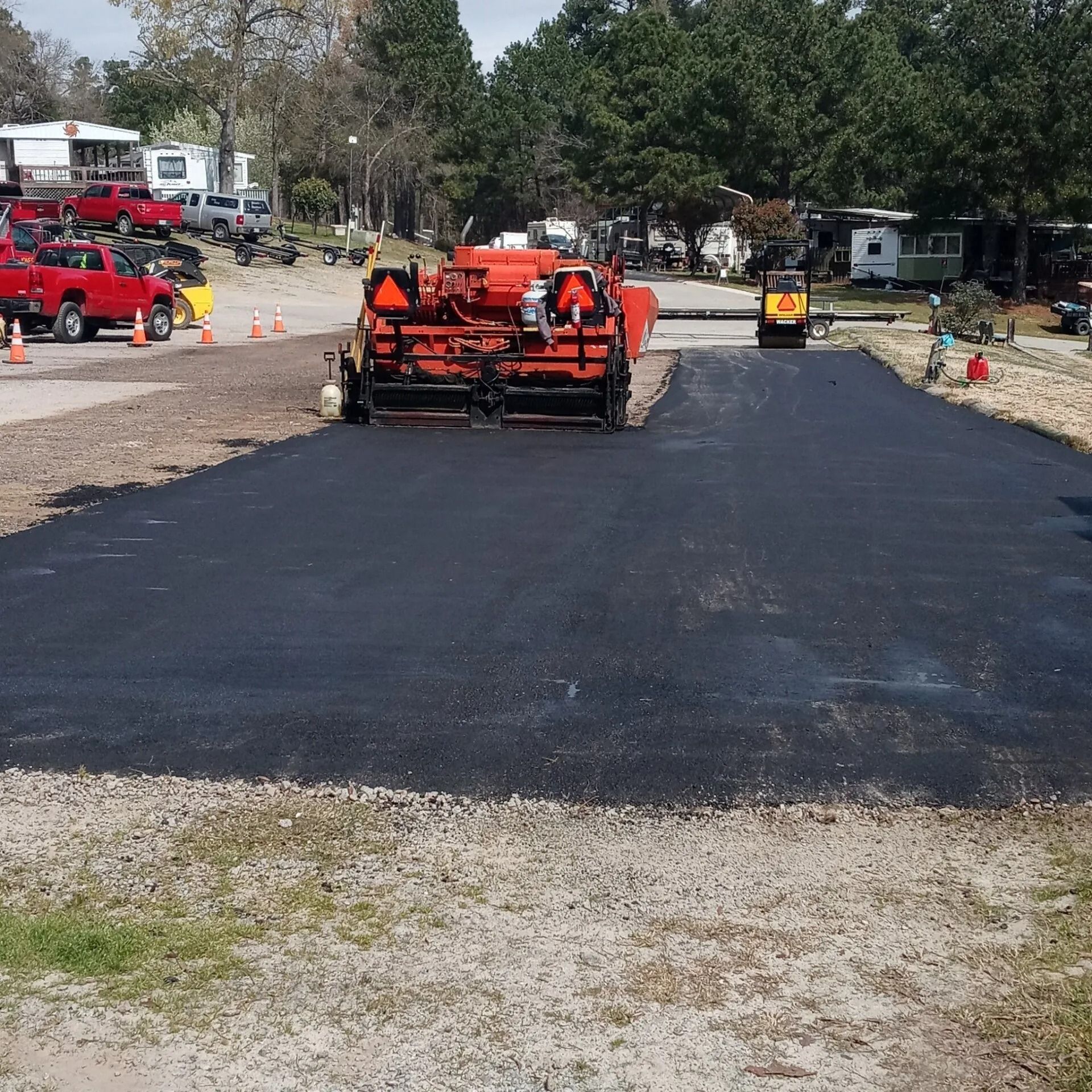 Orange paving machine laying fresh black asphalt on a road under construction outdoors