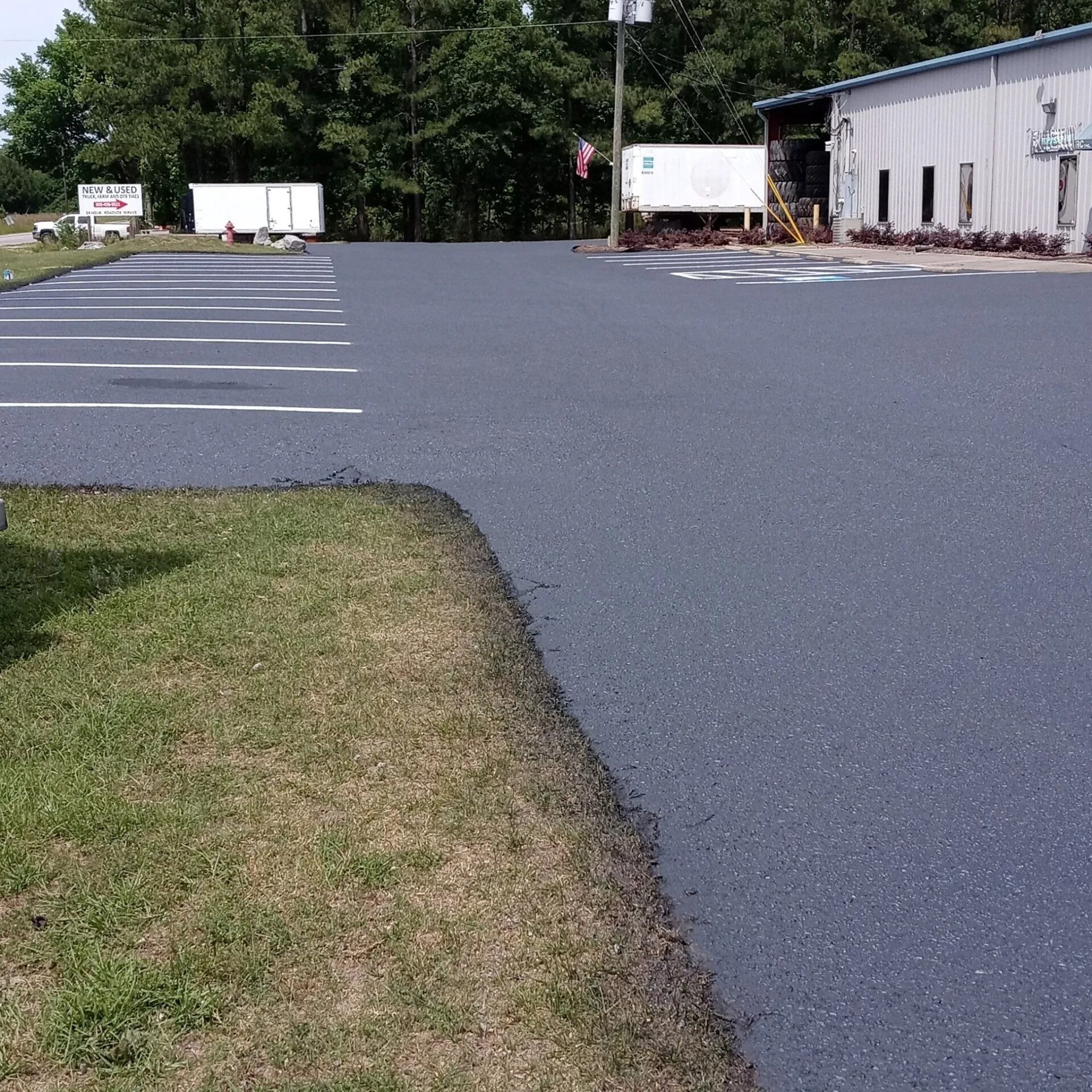 Empty parking lot beside a white building, with trailers and trees in the background.
