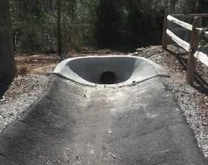 Concrete skate bowl trail feature with a circular opening in a wooded outdoor setting