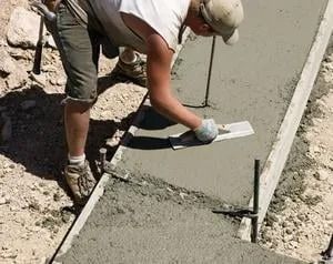 Worker smoothing wet concrete with a trowel along a sidewalk edge