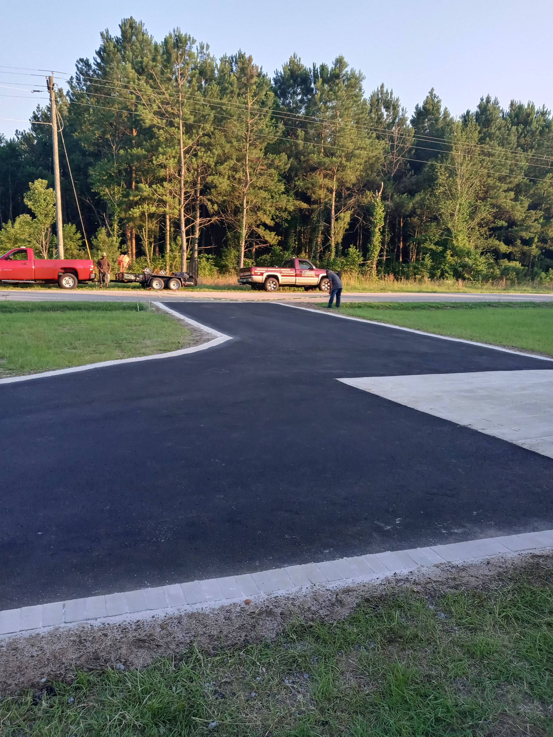 Freshly paved black path curves through a grassy park beside trees and parked vehicles
