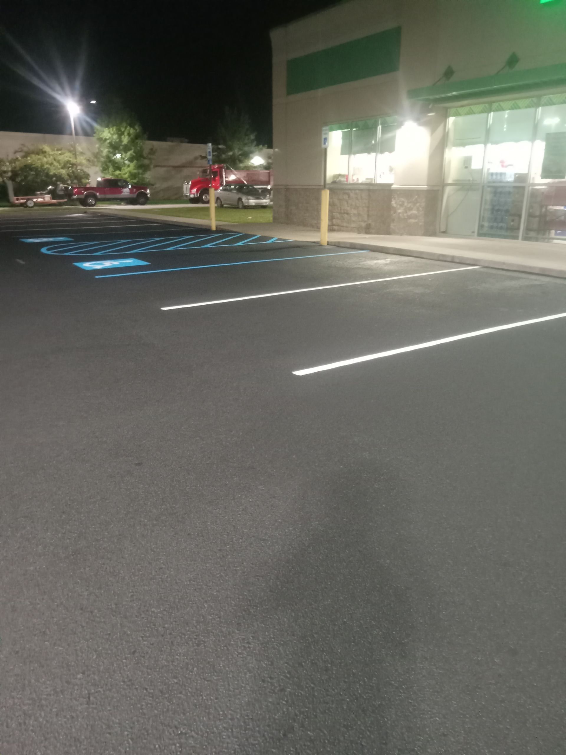 Empty parking lot at night beside a store with green awnings and lit windows