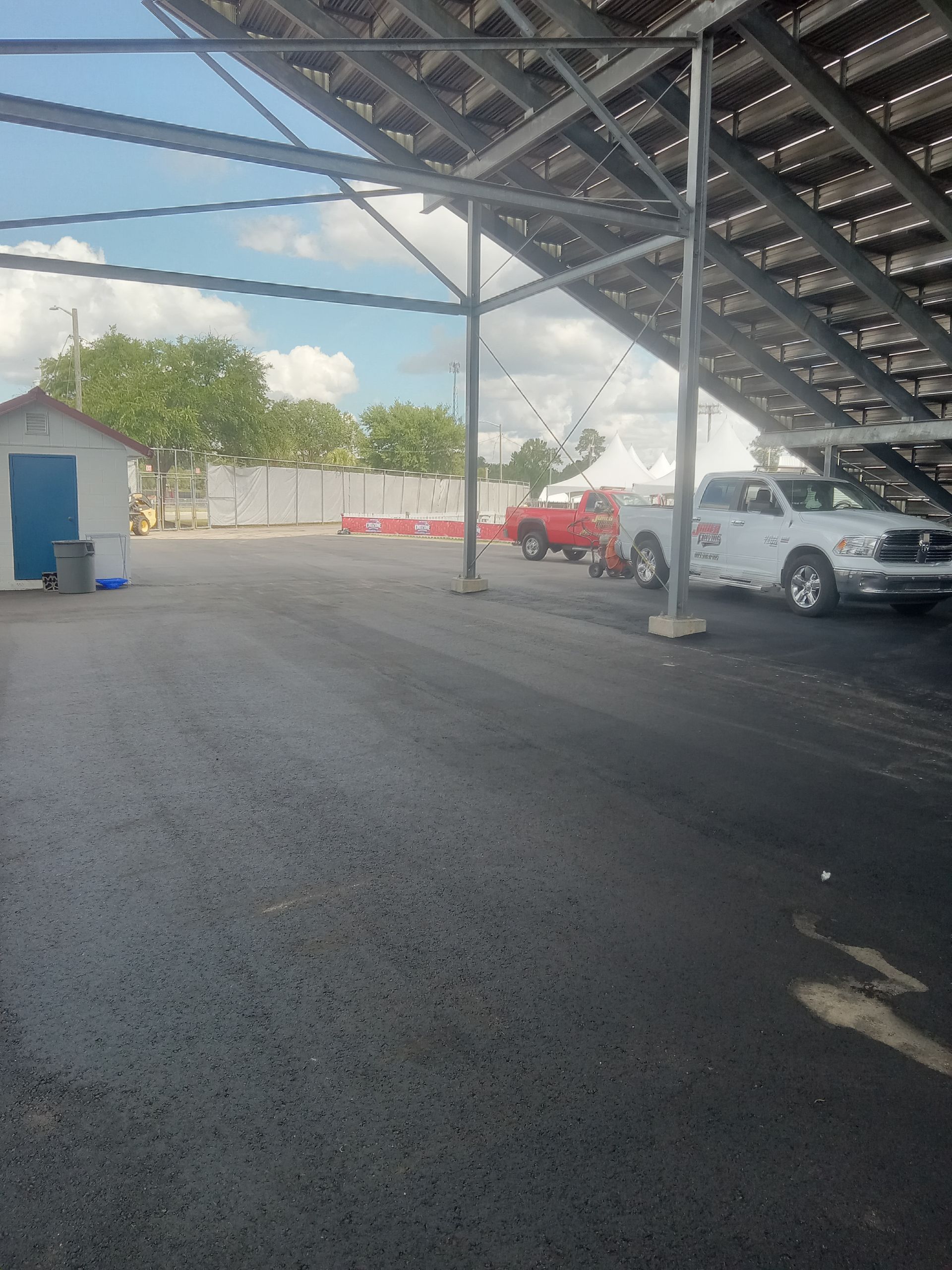 Covered parking lot with a red car and white car under metal stairs, blue sky overhead