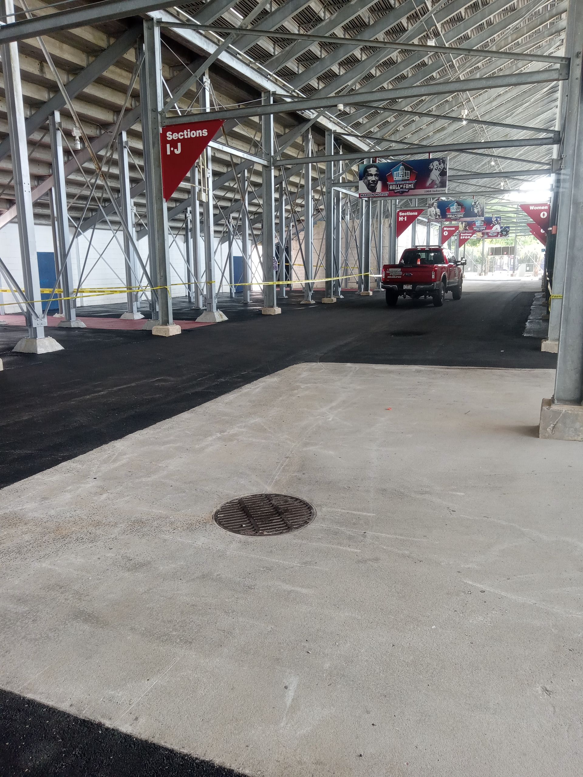 Covered walkway under construction with steel beams, dirt piles, a red utility cart, and concrete floor.
