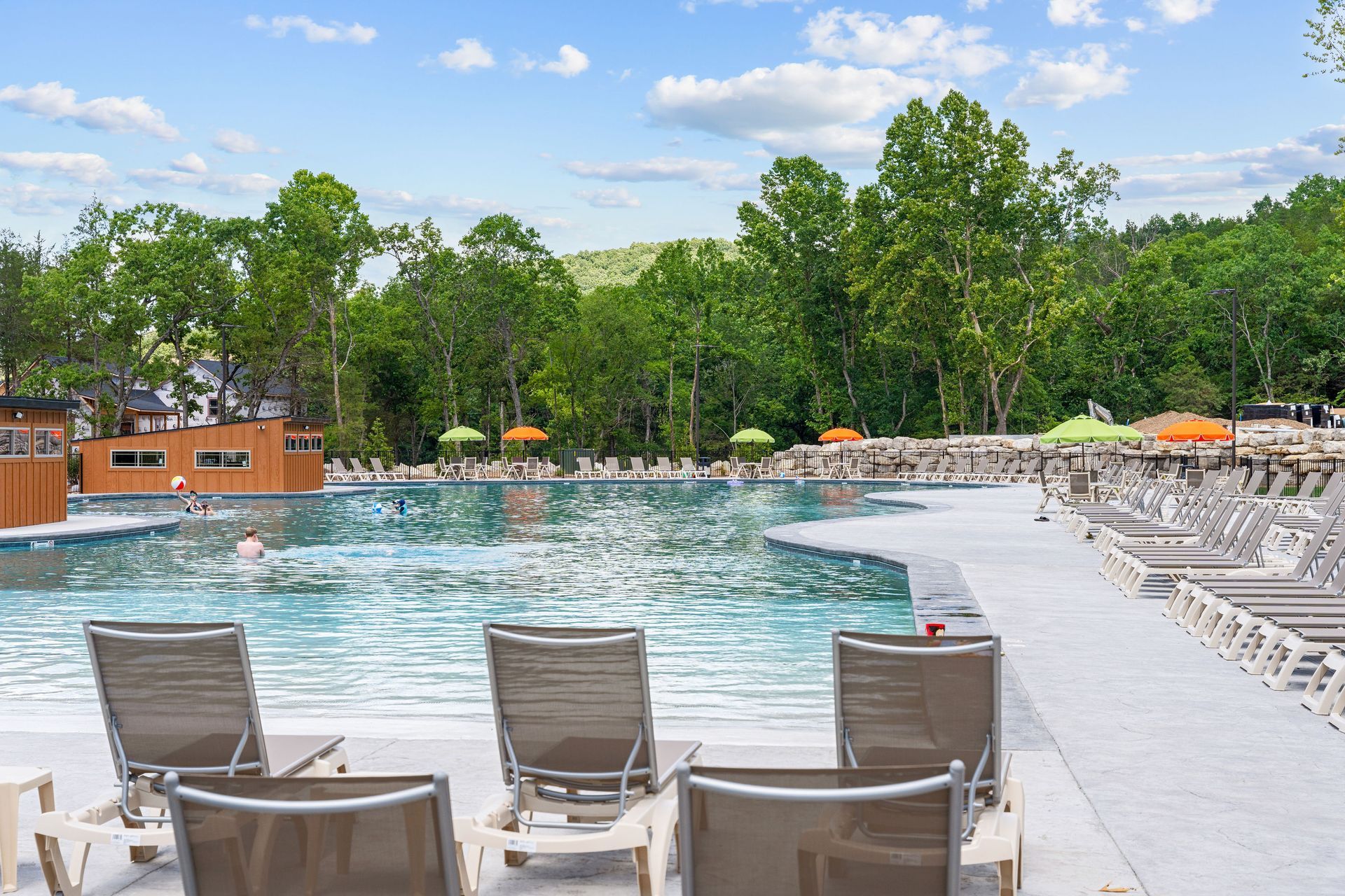 Outdoor pool with lounge chairs, umbrellas, and trees under a blue sky