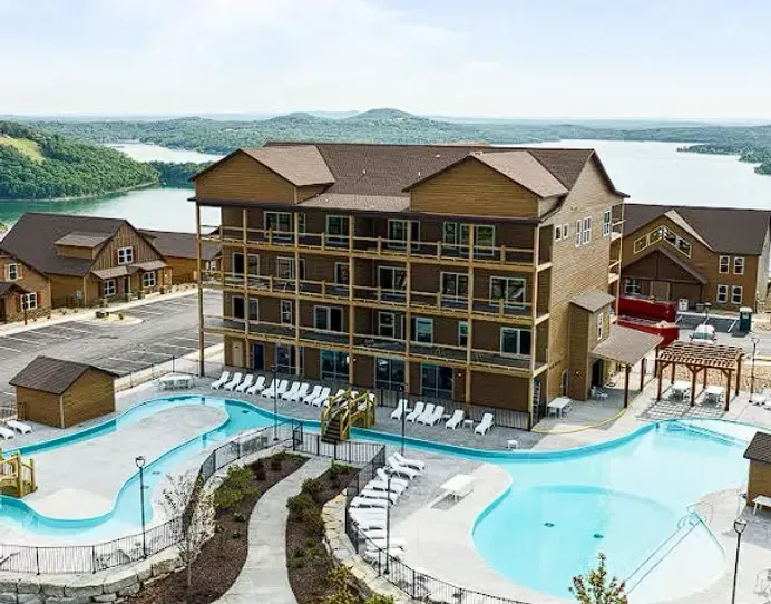 Lakeside resort with pool, multi-story lodge, and surrounding patios under cloudy skies