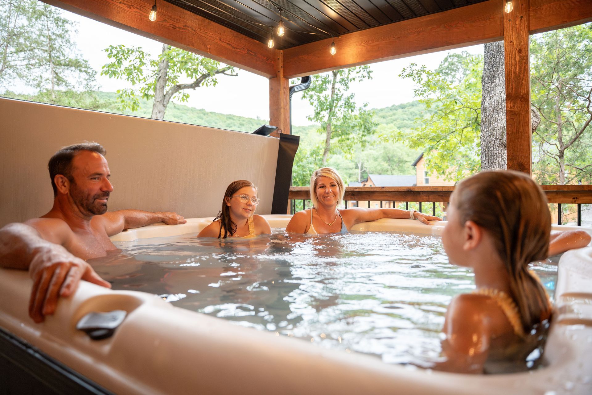 People relaxing in an indoor hot tub under a covered wooden pavilion, with trees visible outside.