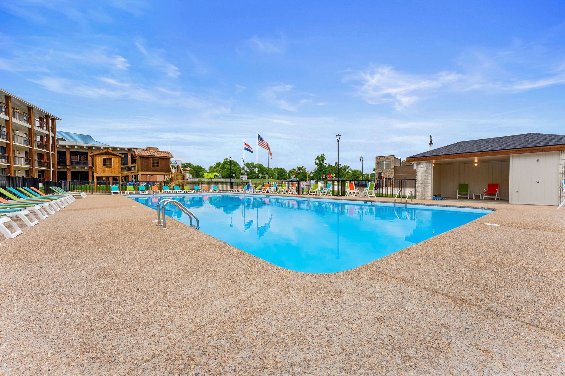 Resort-style outdoor pool with blue water, lounge chairs, and tan buildings under a clear sky
