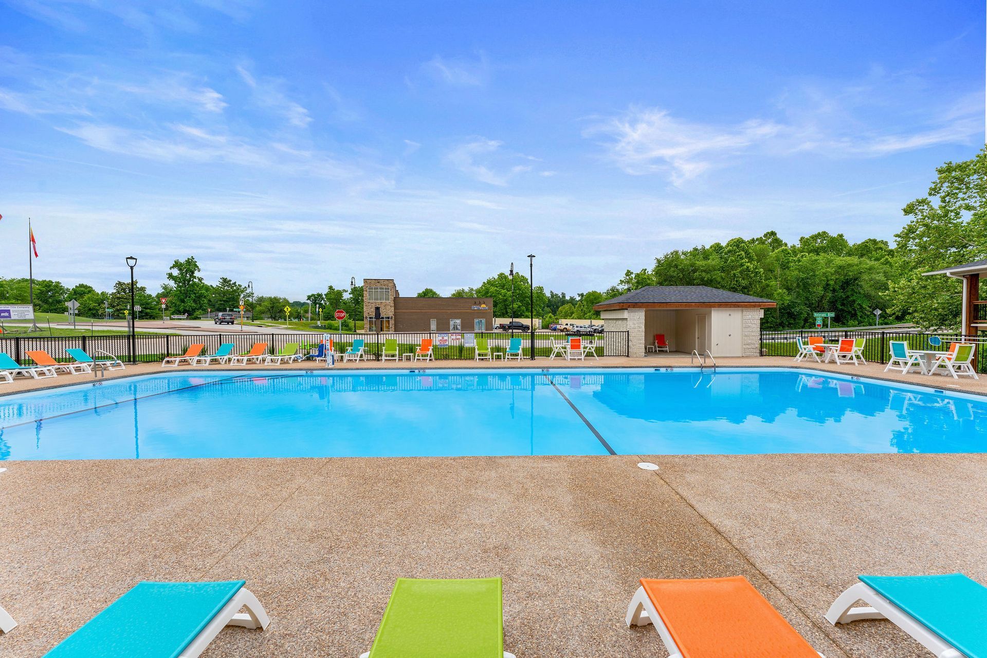 Outdoor swimming pool with blue water, colorful lounge chairs, and a clear sky