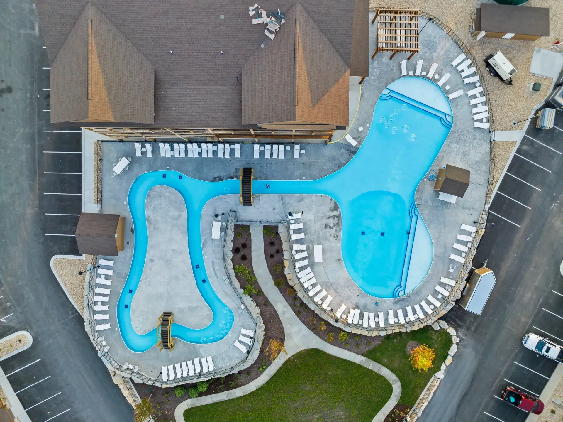 Aerial view of a resort pool with bright blue water, lounge chairs, and a surrounding deck near buildings.