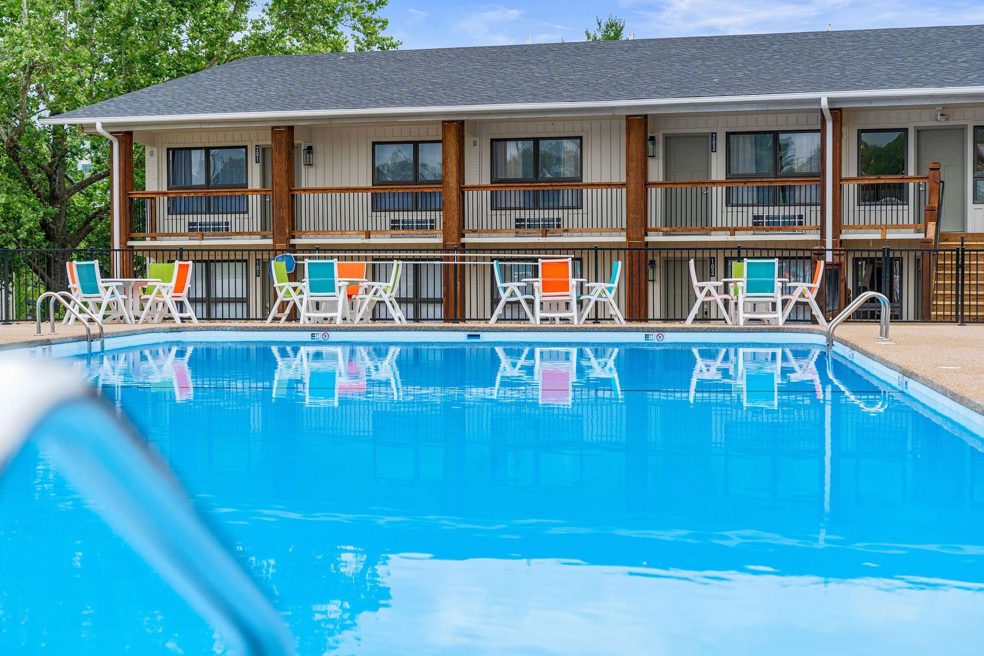 Motel pool with blue water, lounge chairs, and rooms in the background