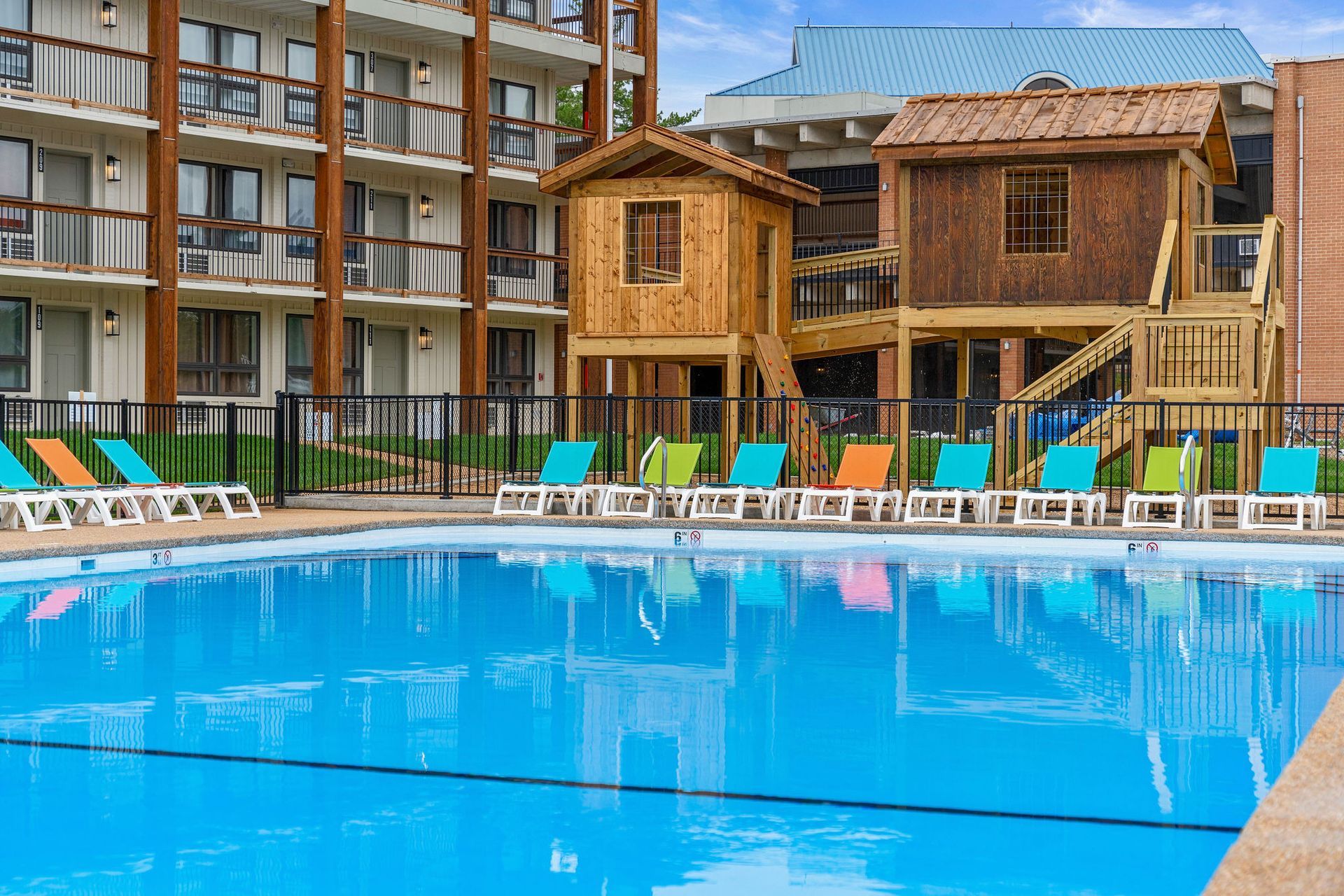 Resort pool with lounge chairs, wooden cabanas, and apartment balconies in the background