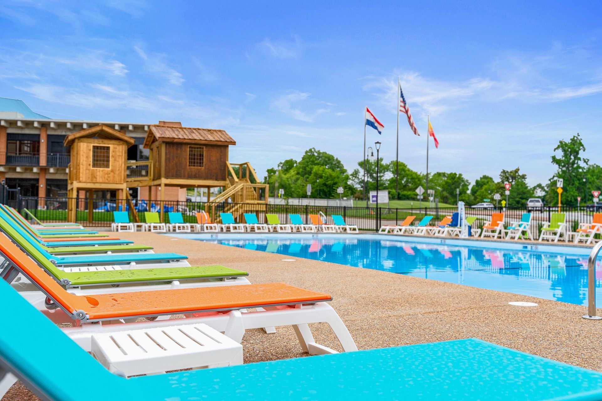 Resort pool with colorful lounge chairs, blue water, and a wooden lodge under a bright sky