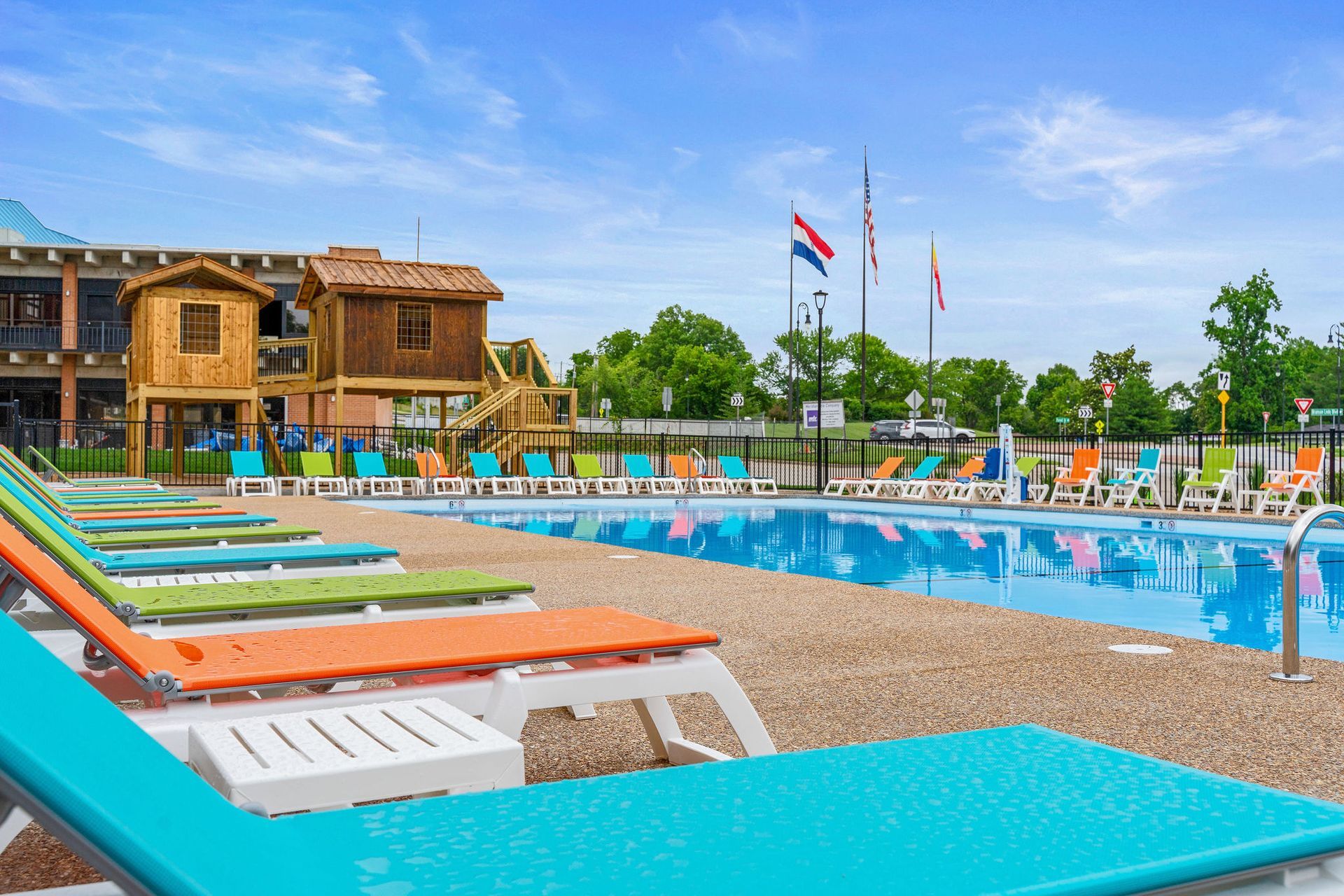 Colorful poolside lounge chairs beside a clear blue swimming pool and wooden resort building under a sunny sky