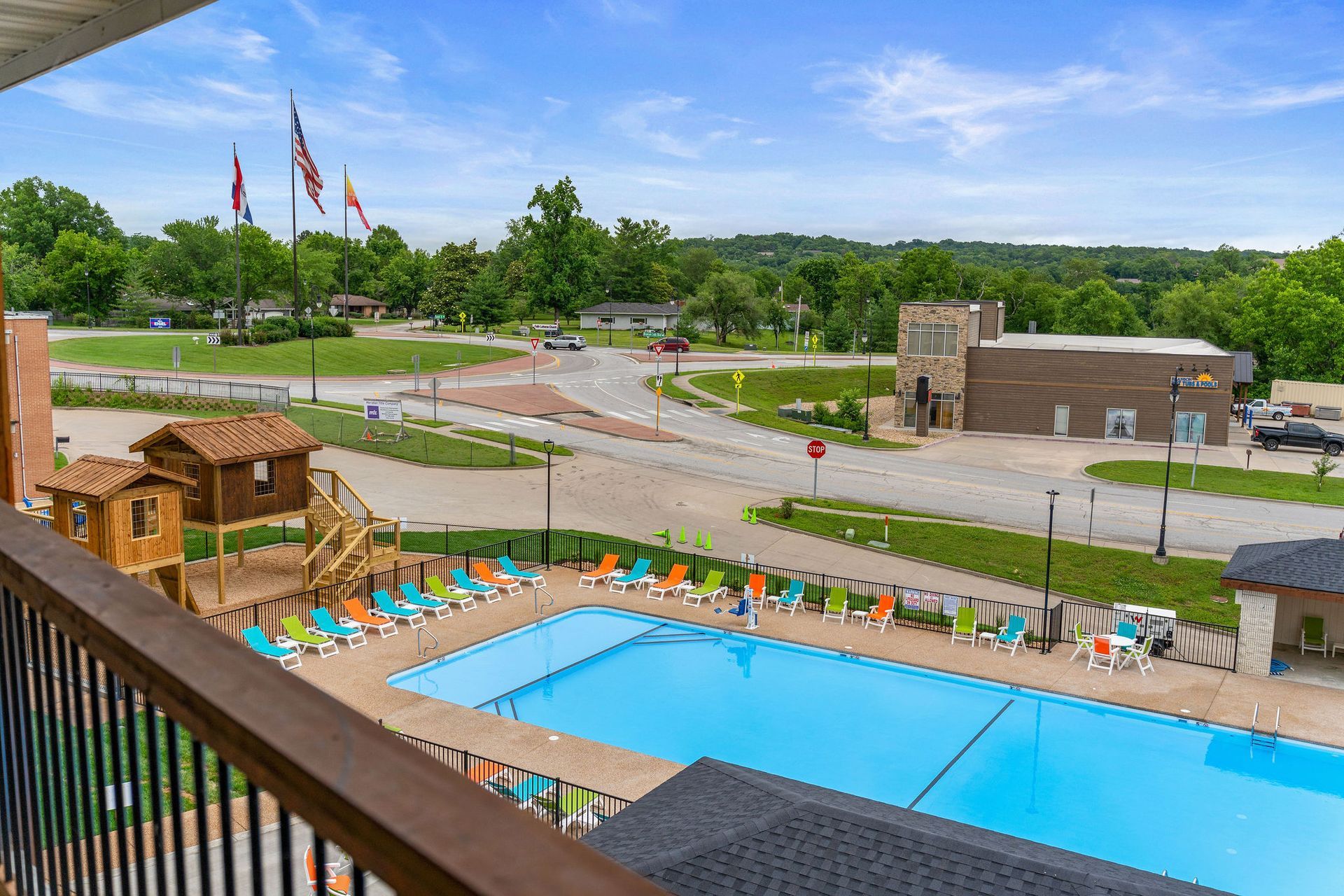 Outdoor resort pool with lounge chairs, pergola, and a landscaped road view under a cloudy sky