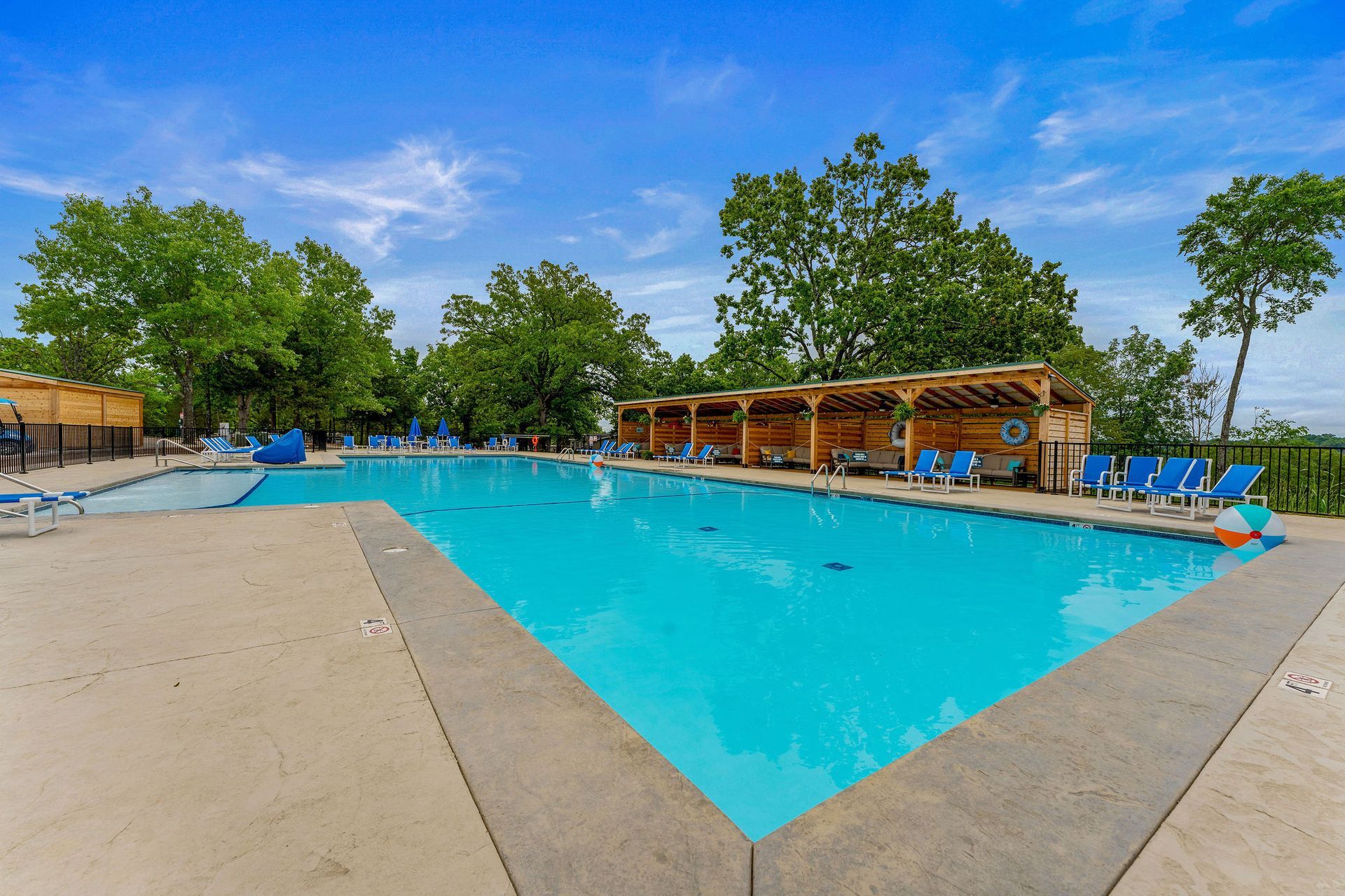 Outdoor swimming pool with bright blue water, lounge chairs, and trees under a clear sky