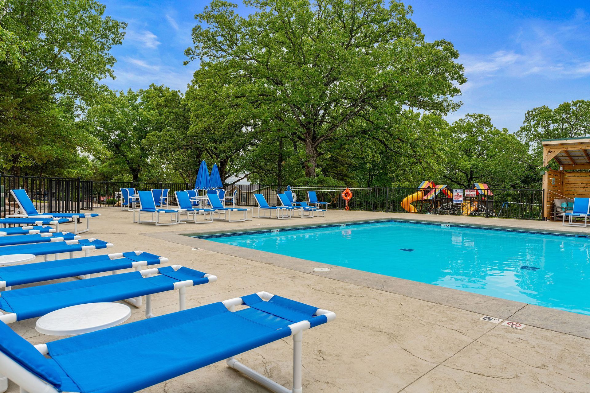 Outdoor pool with blue lounge chairs and trees in the background