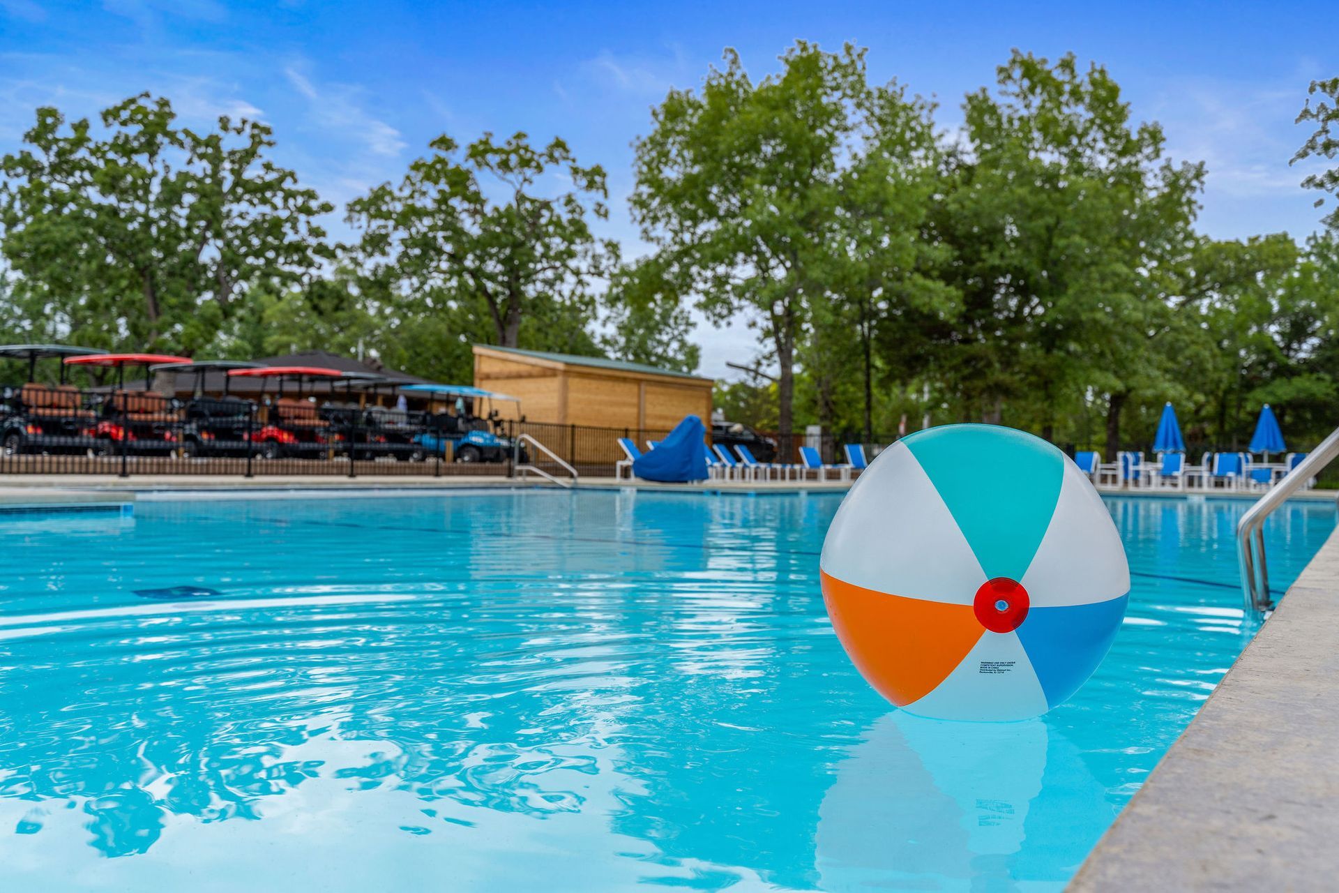 Outdoor swimming pool with a large beach ball floating near the edge under a sunny blue sky