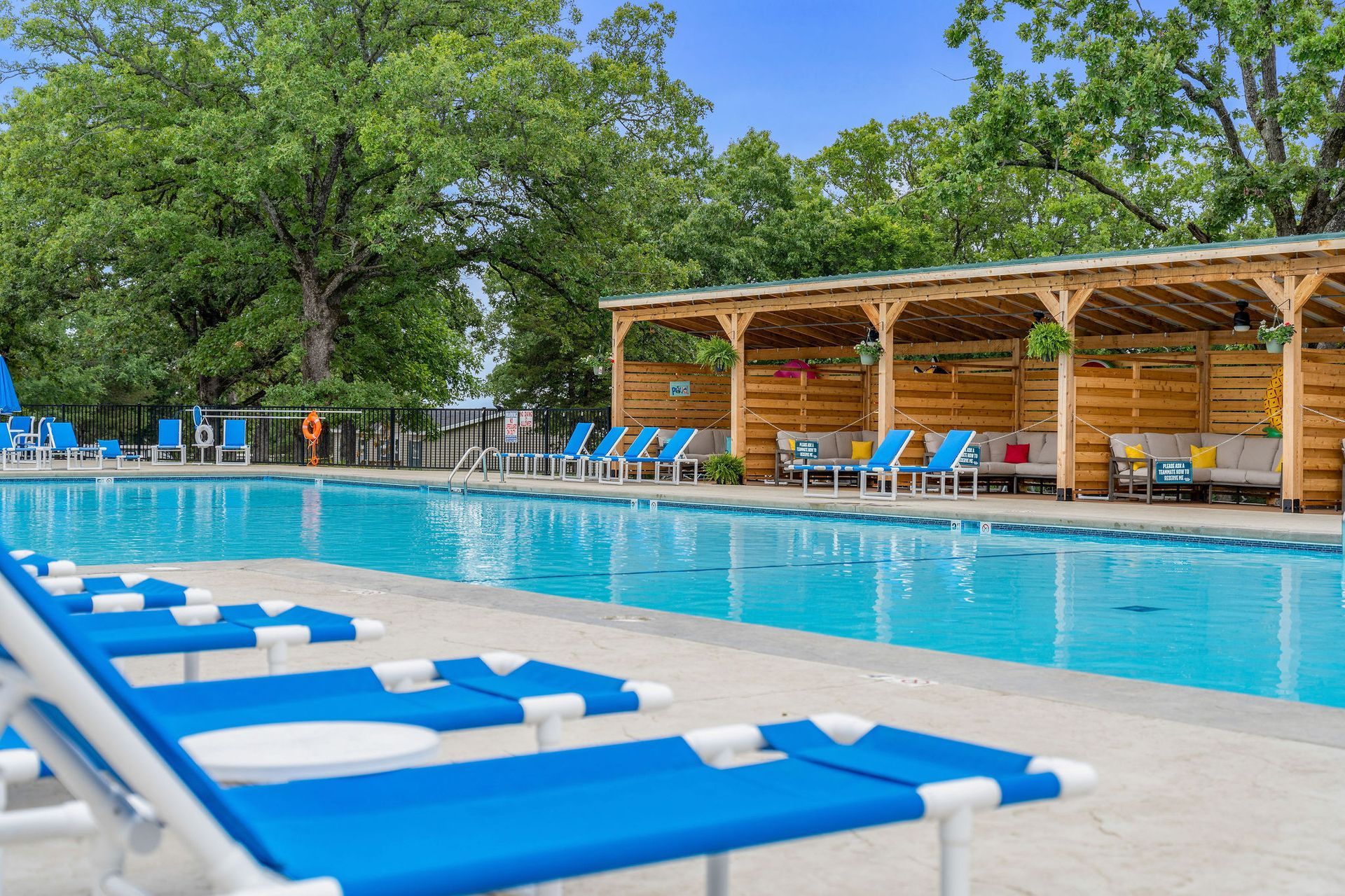 Outdoor swimming pool with blue lounge chairs and a wooden cabana under trees