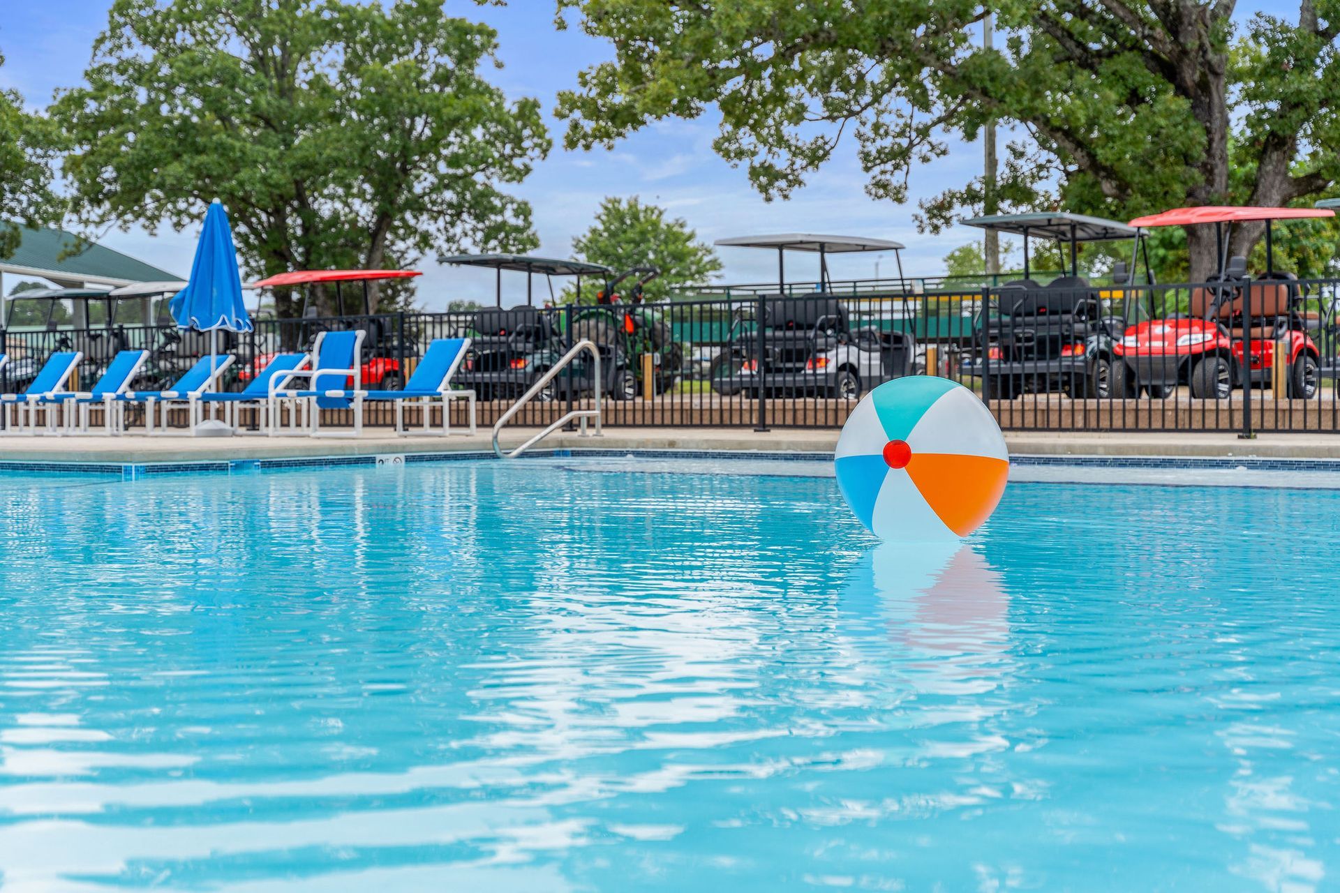 Outdoor pool with blue lounge chairs, umbrellas, and a colorful beach ball floating in the water