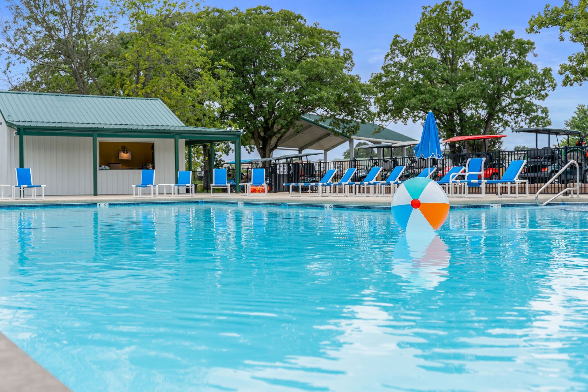 Outdoor swimming pool with blue water, lounge chairs, and a small building under trees