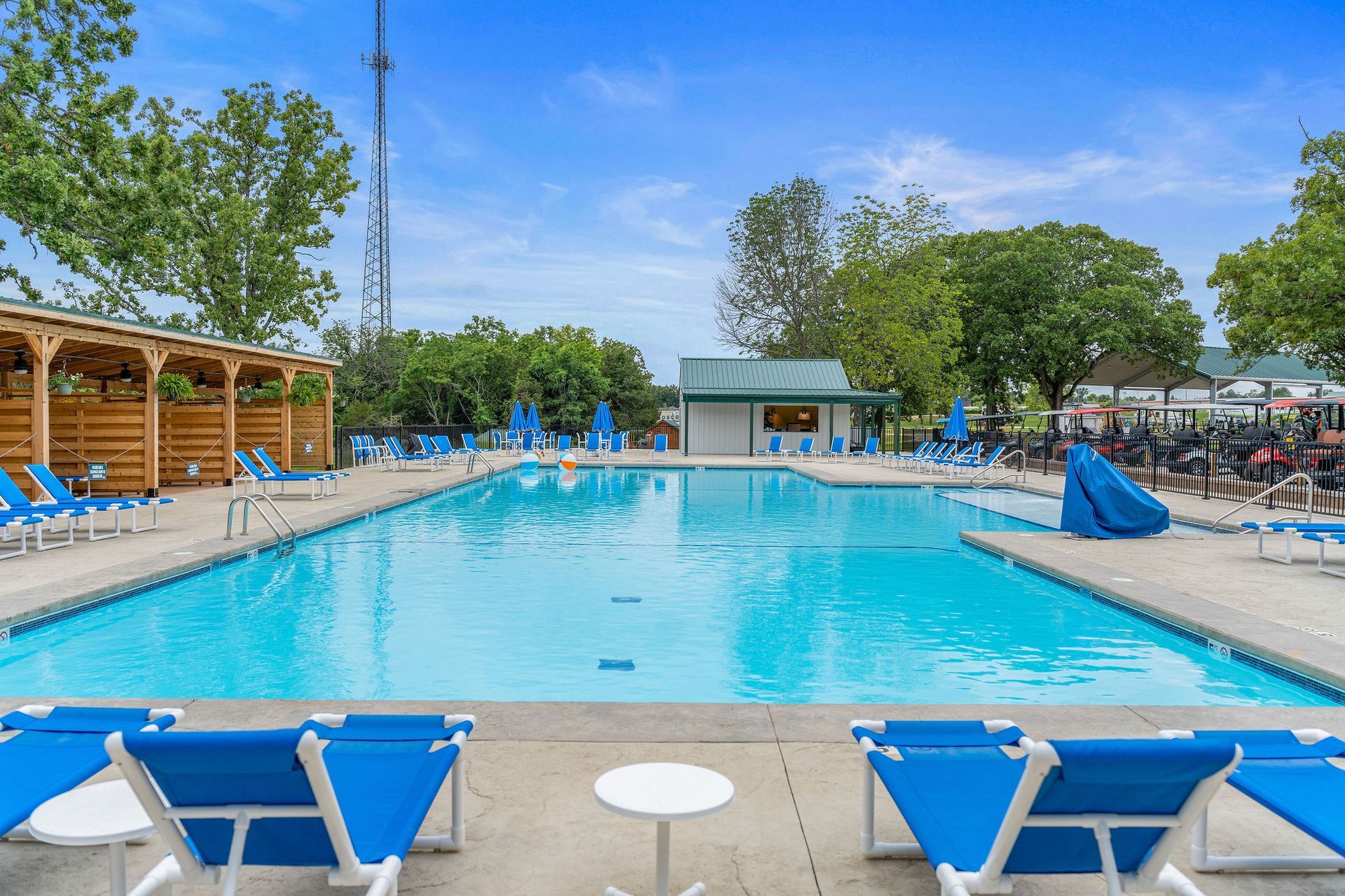 Outdoor swimming pool with blue lounge chairs, umbrellas, and trees on a sunny day