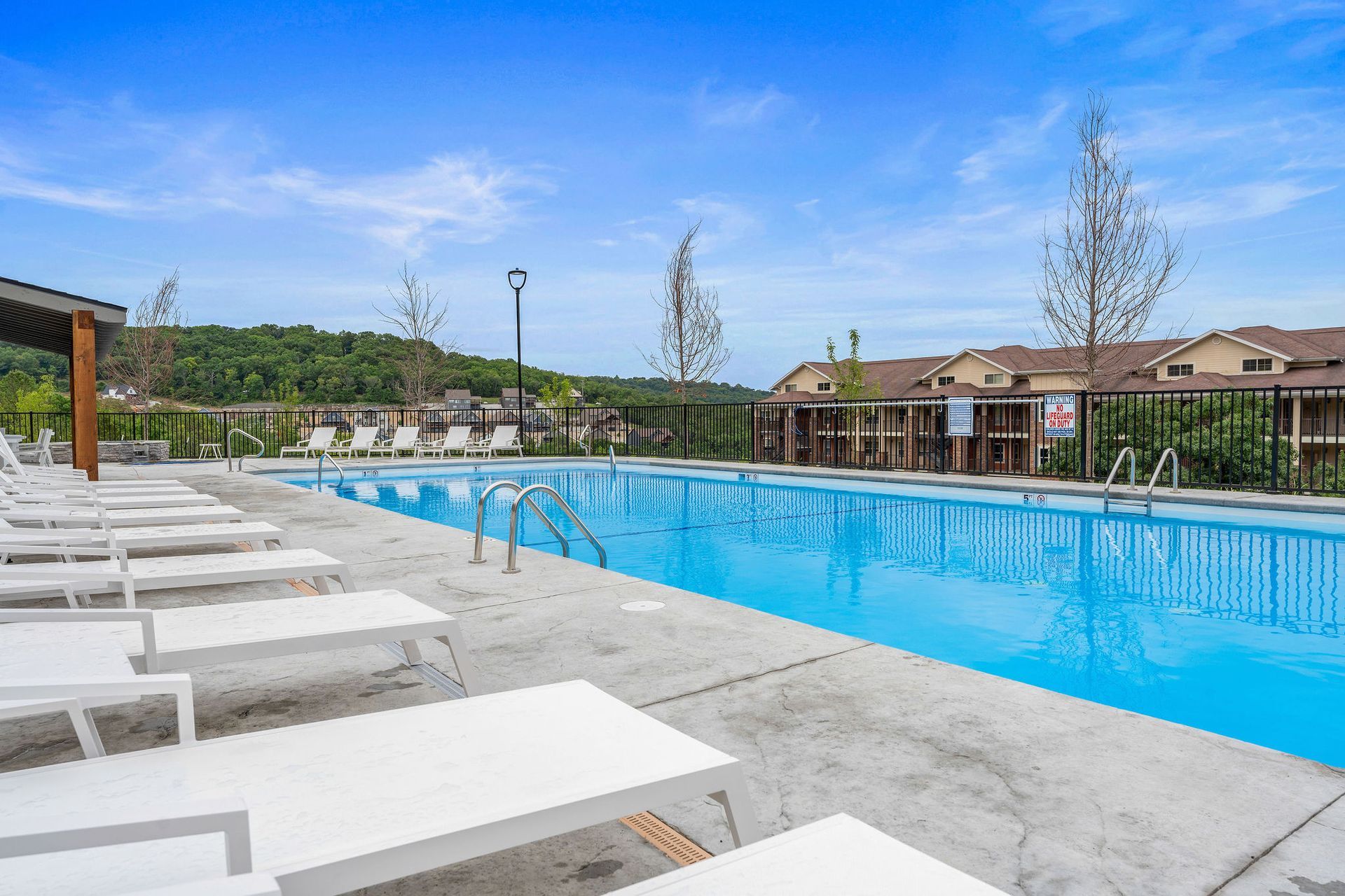 Outdoor swimming pool with blue water, white lounge chairs, and a row of brick townhouses under a clear sky