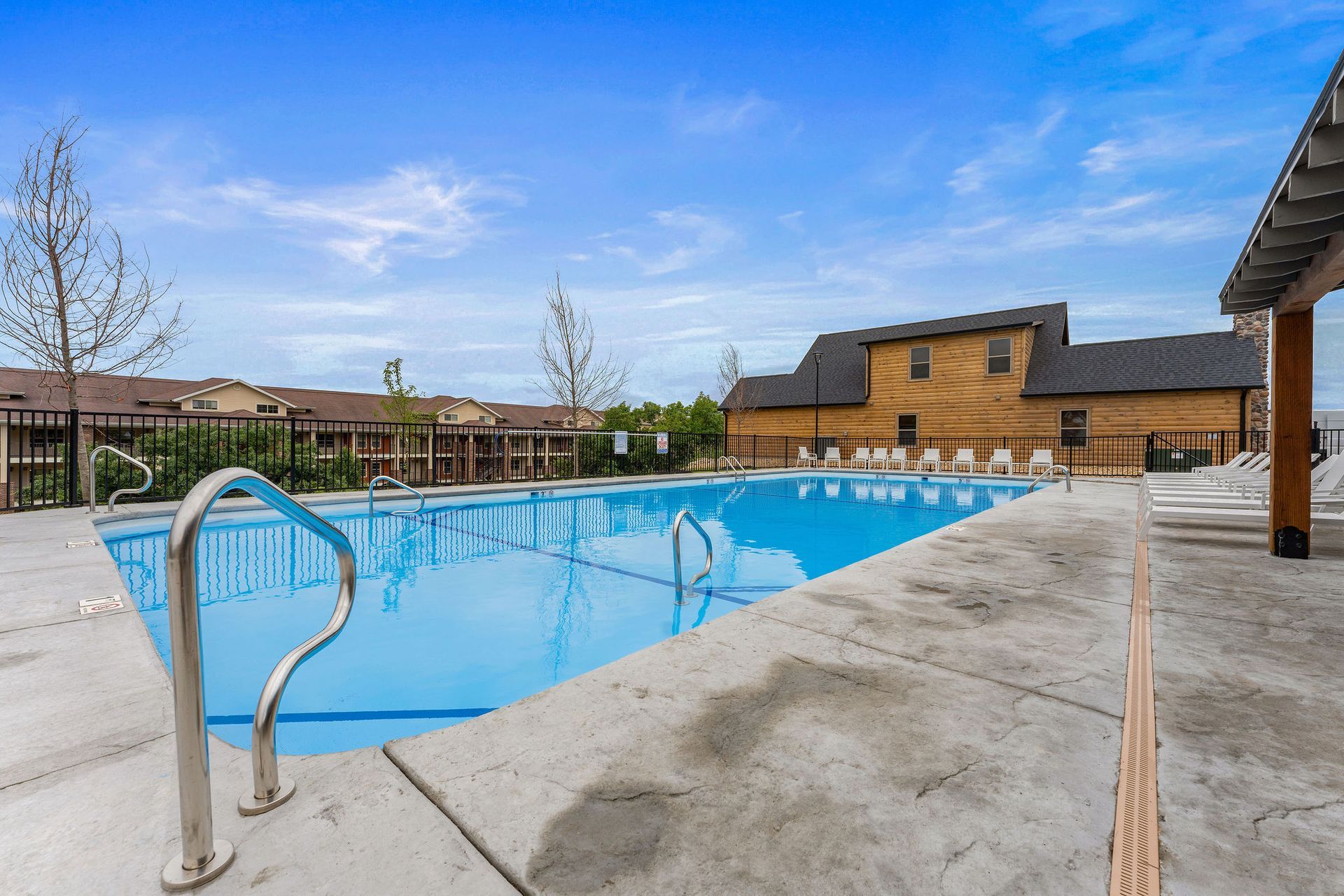 Outdoor apartment complex swimming pool with blue water, concrete deck, and surrounding buildings under a clear sky