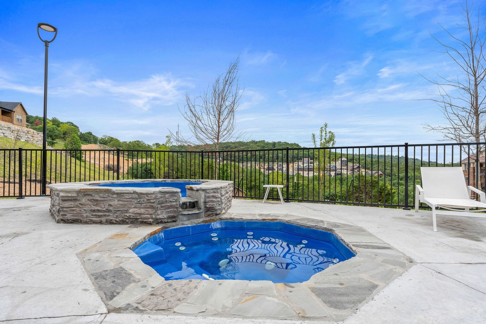 Small stone hot tub or spa beside a patio with black fence and blue sky background