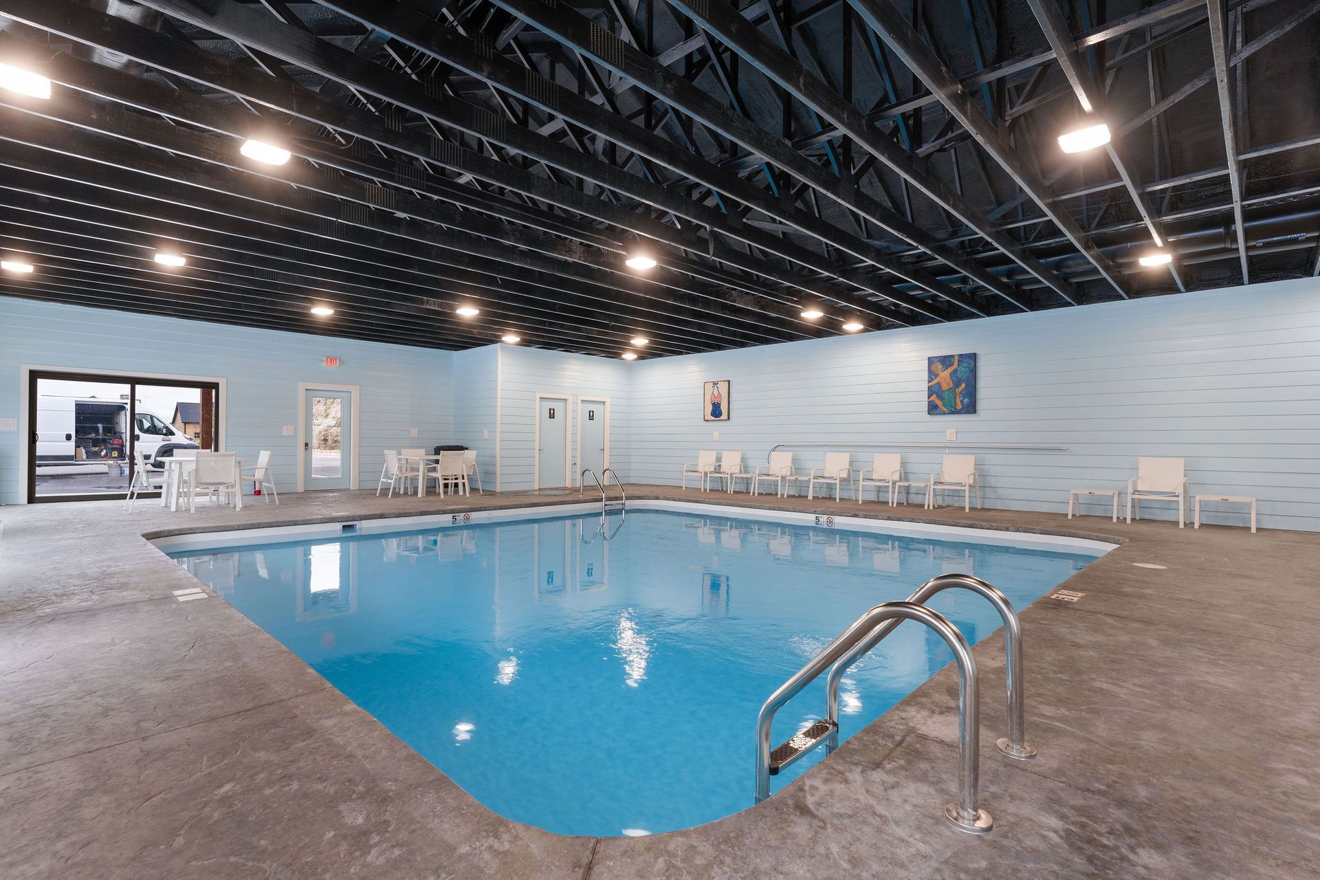 Indoor swimming pool with blue water, white lounge chairs, and dark exposed ceiling beams