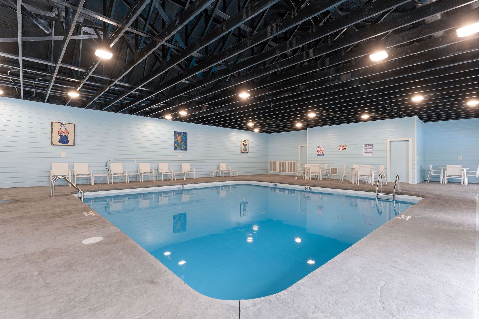 Indoor swimming pool with blue water, white chairs, and a black ceiling