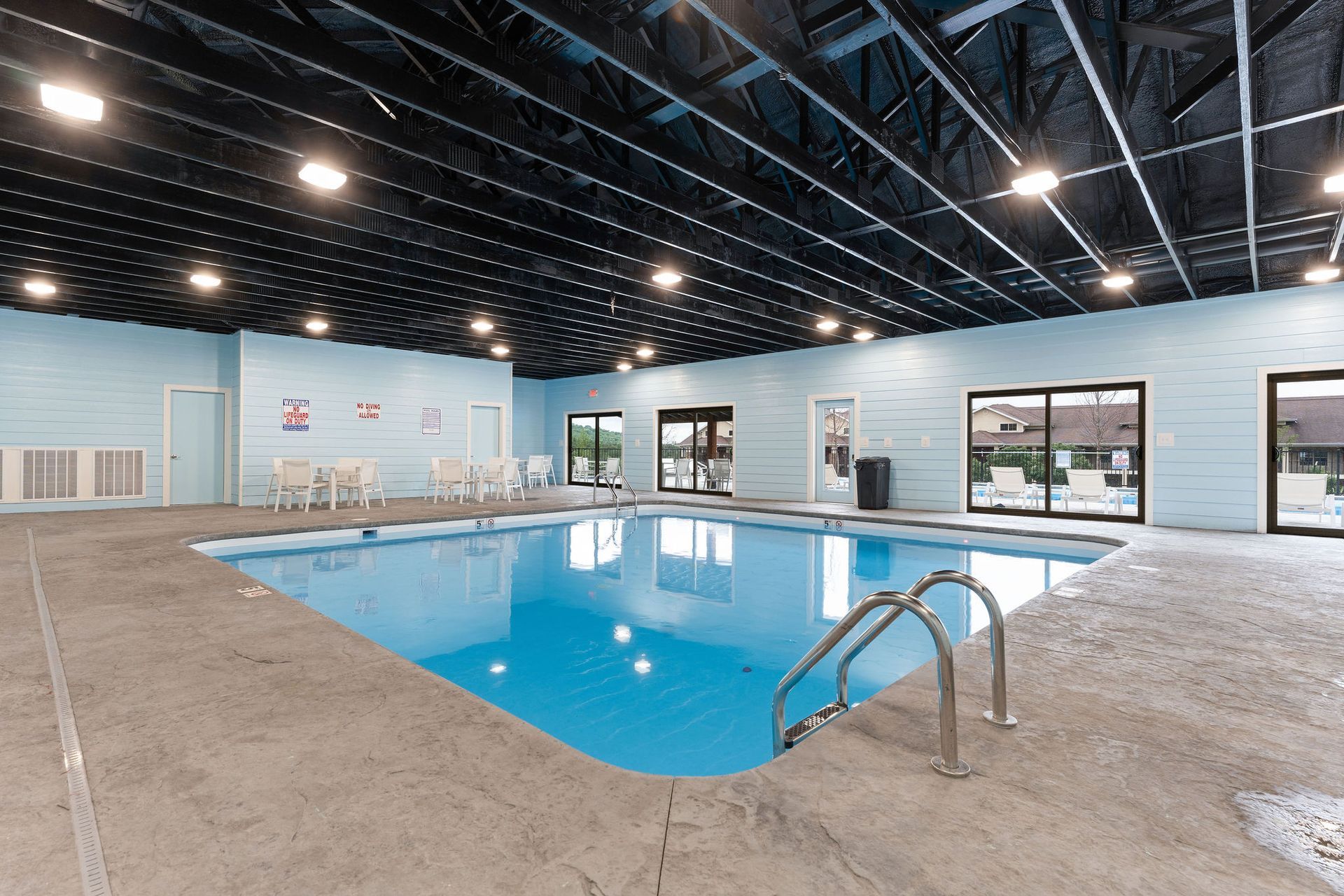 Indoor swimming pool with blue water, tan deck, and large windows under a black ceiling.