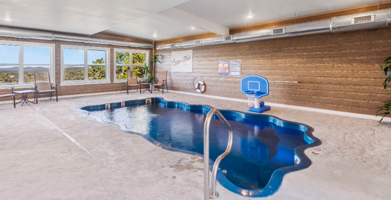 Indoor pool room with a blue pool and a mini basketball hoop, surrounded by windows and wood-paneled walls
