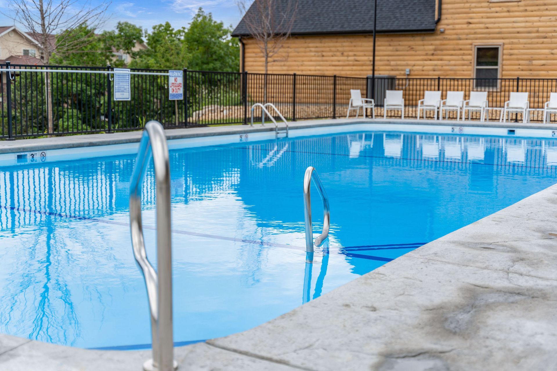 Outdoor swimming pool with blue water, metal handrails, and a wooden building in the background