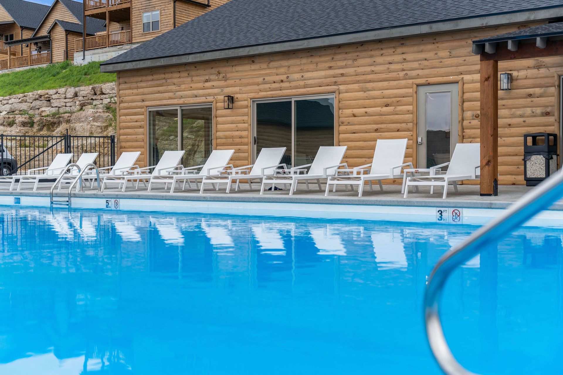 Outdoor pool with blue water, white lounge chairs, and a wooden building in the background