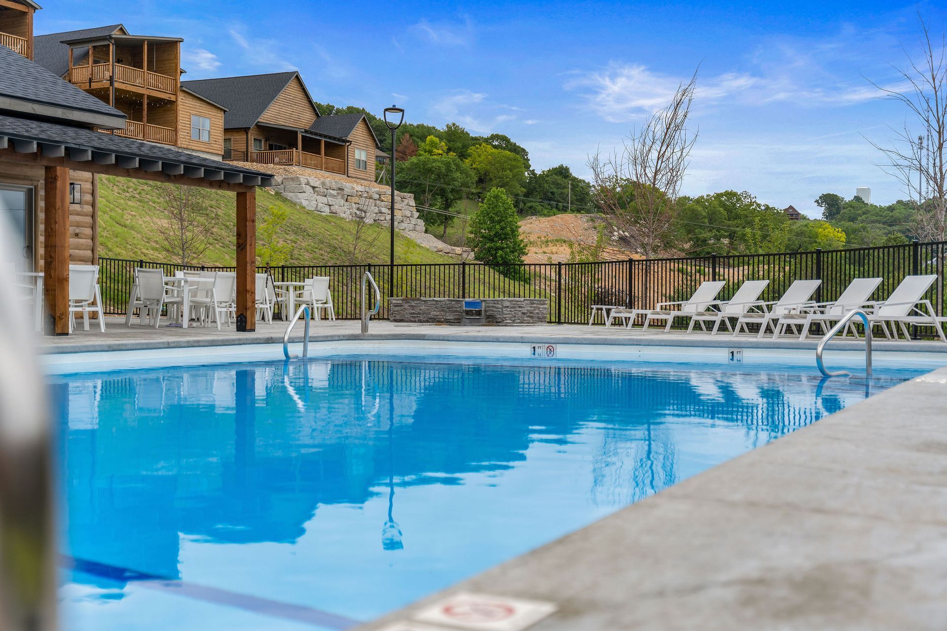 Outdoor resort pool with blue water, lounge chairs, and a wooden building under a clear sky