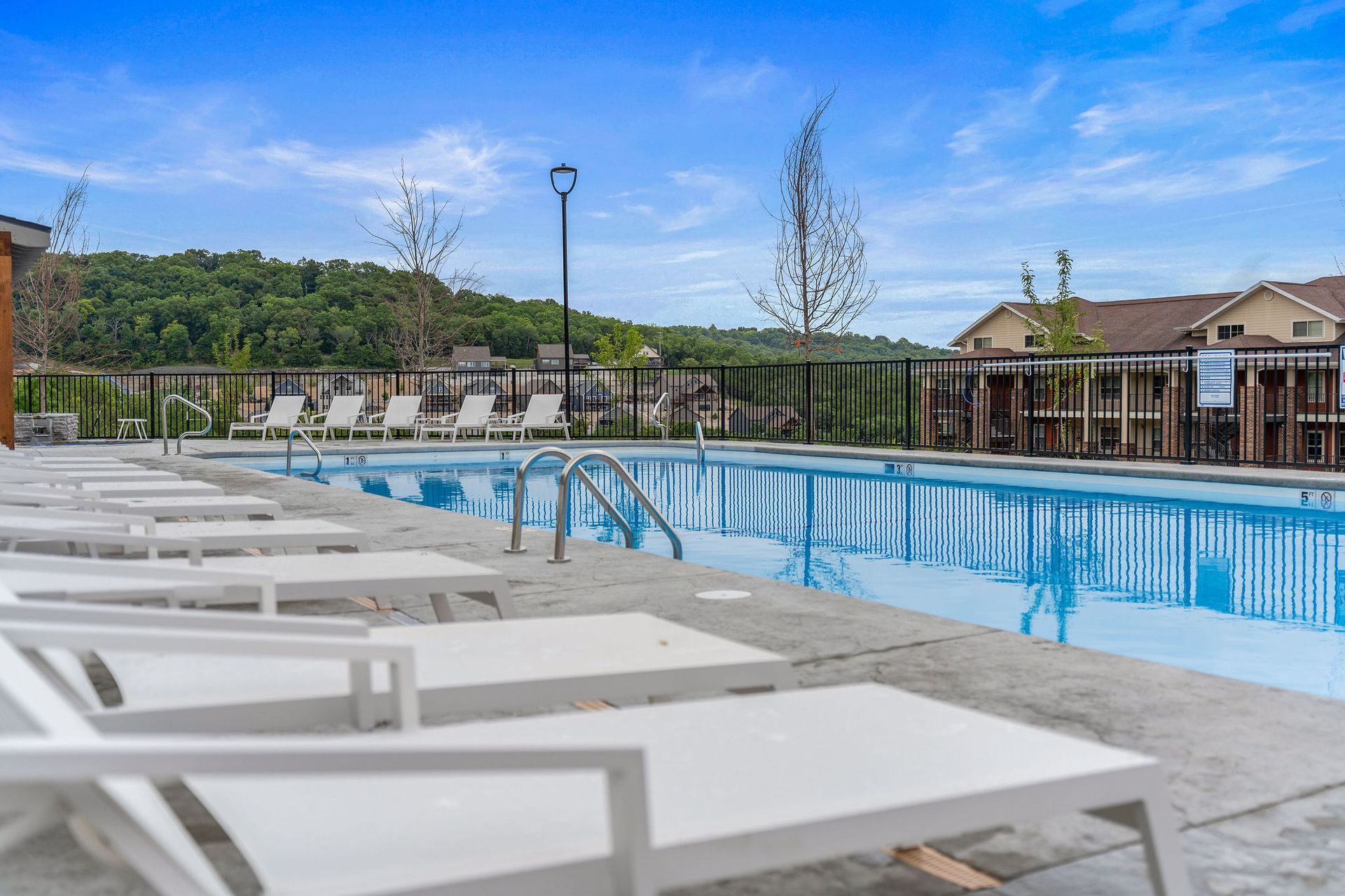 Outdoor pool with white lounge chairs, blue water, and a sunny landscaped patio.