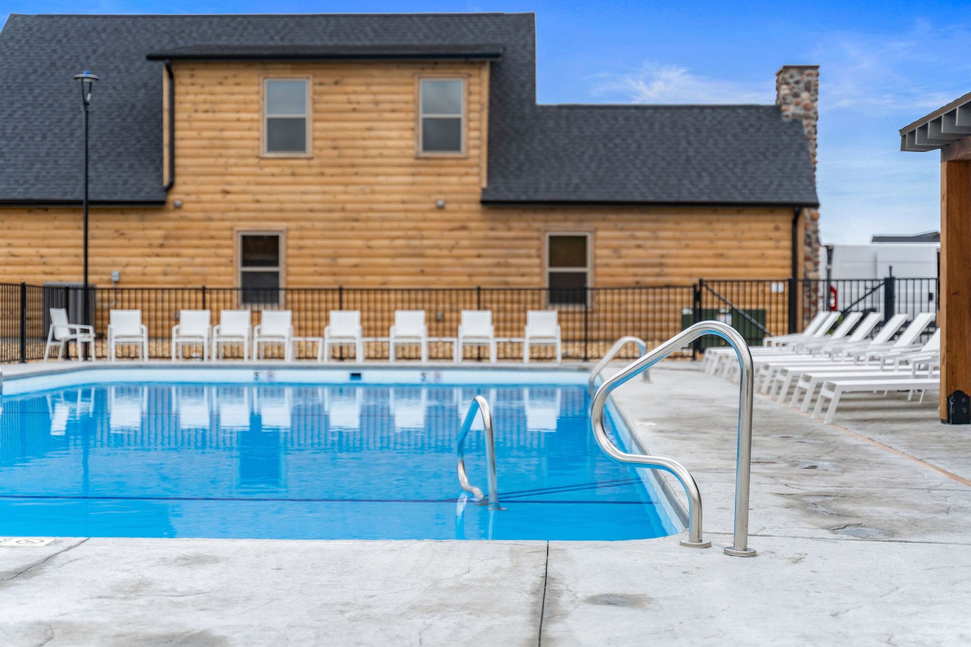 Outdoor swimming pool with white lounge chairs and a wood-sided building in the background