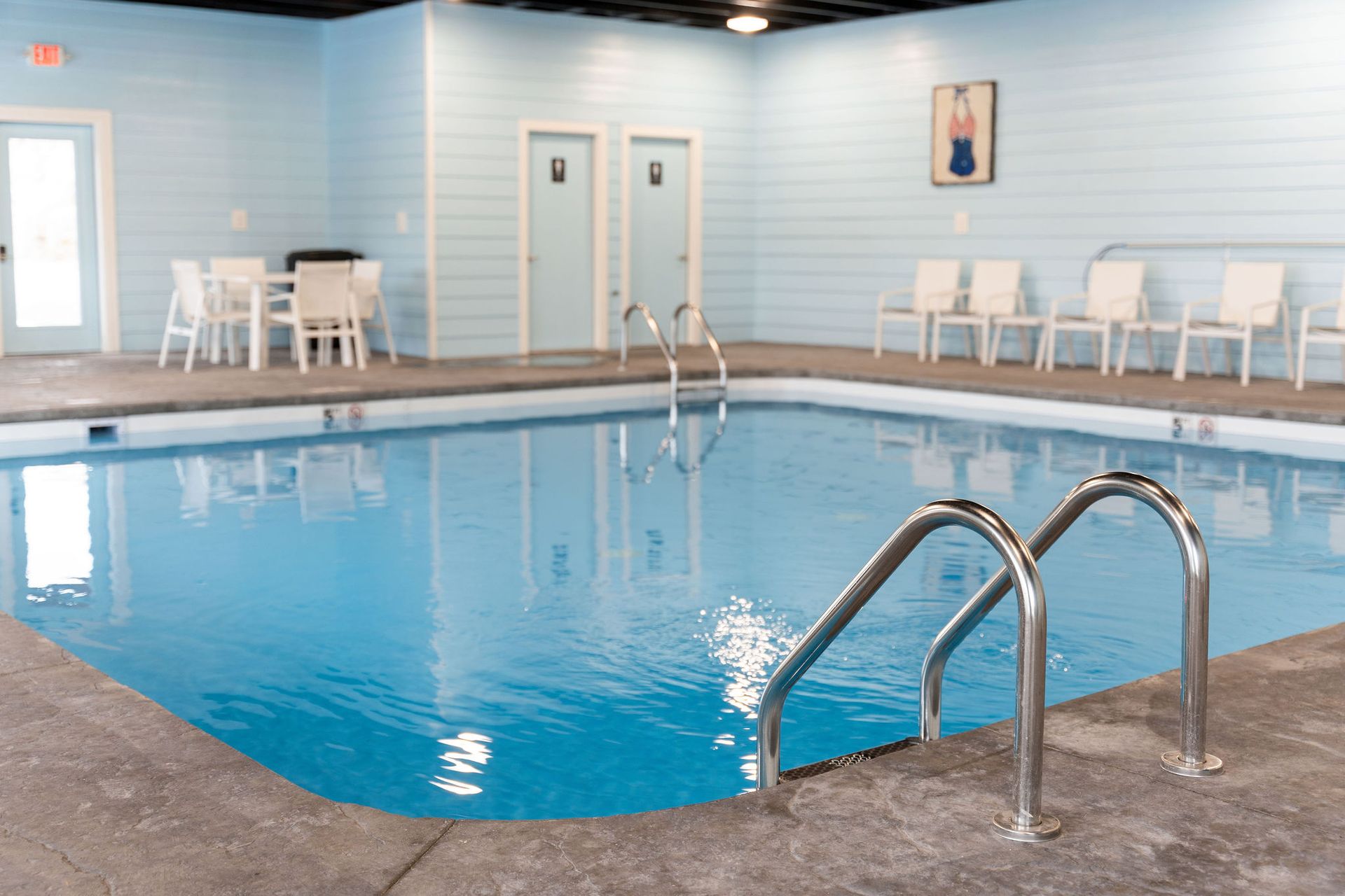 Indoor swimming pool with blue water, metal handrails, and white lounge chairs along the far wall