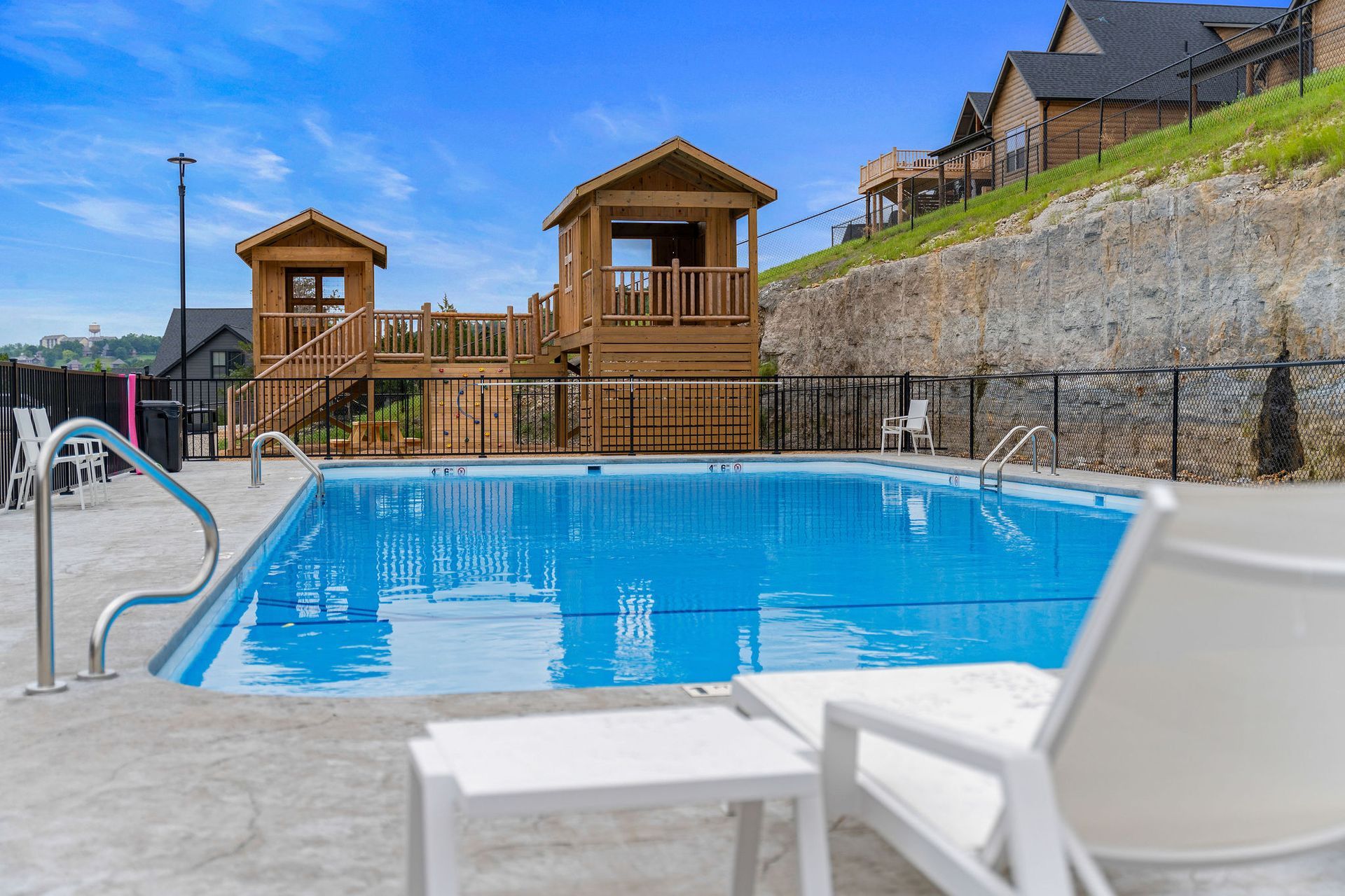 Outdoor pool with blue water, white lounge chairs, and wooden cabanas beside a stone hillside.