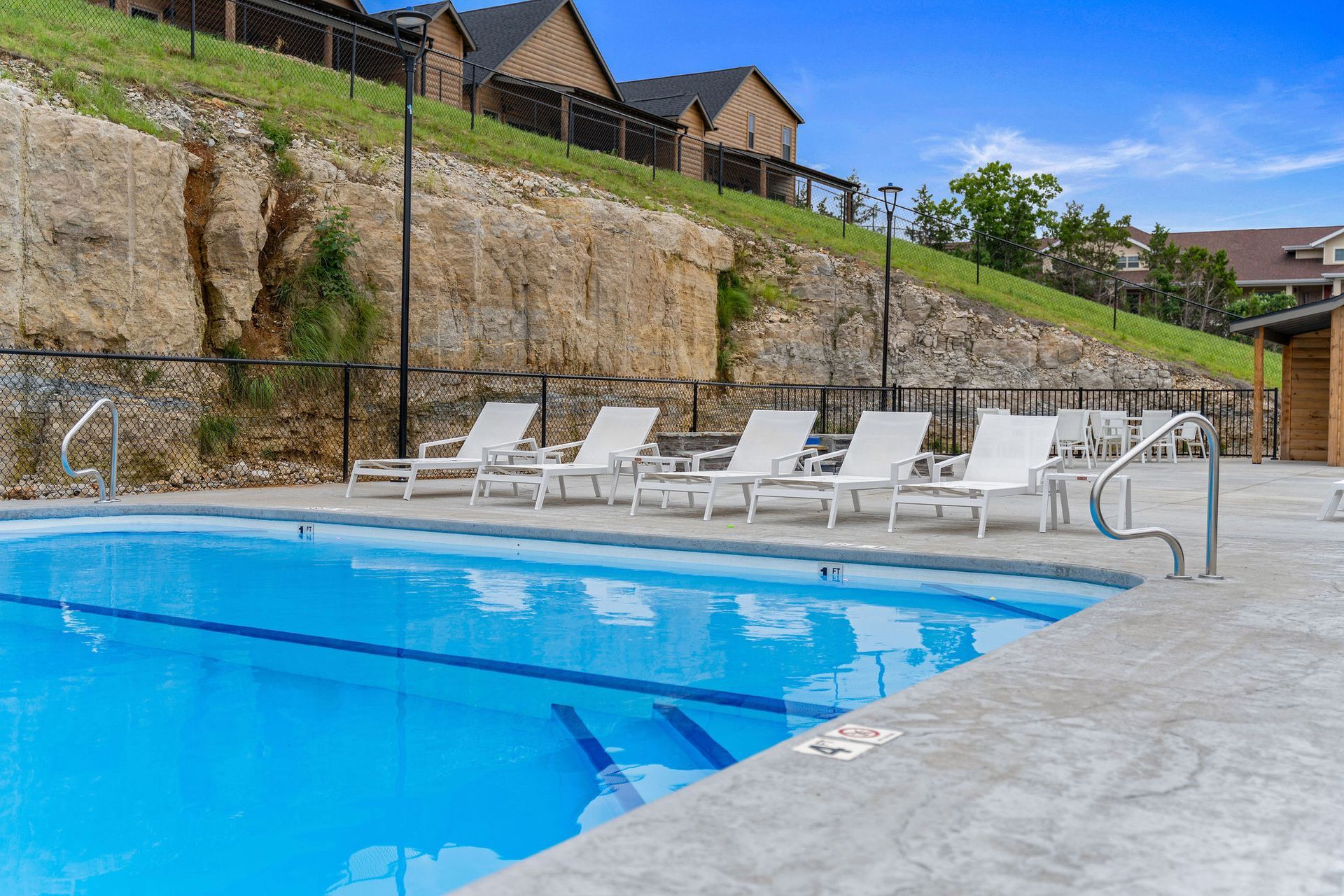 Outdoor swimming pool with white lounge chairs beside a stone deck and hillside backdrop