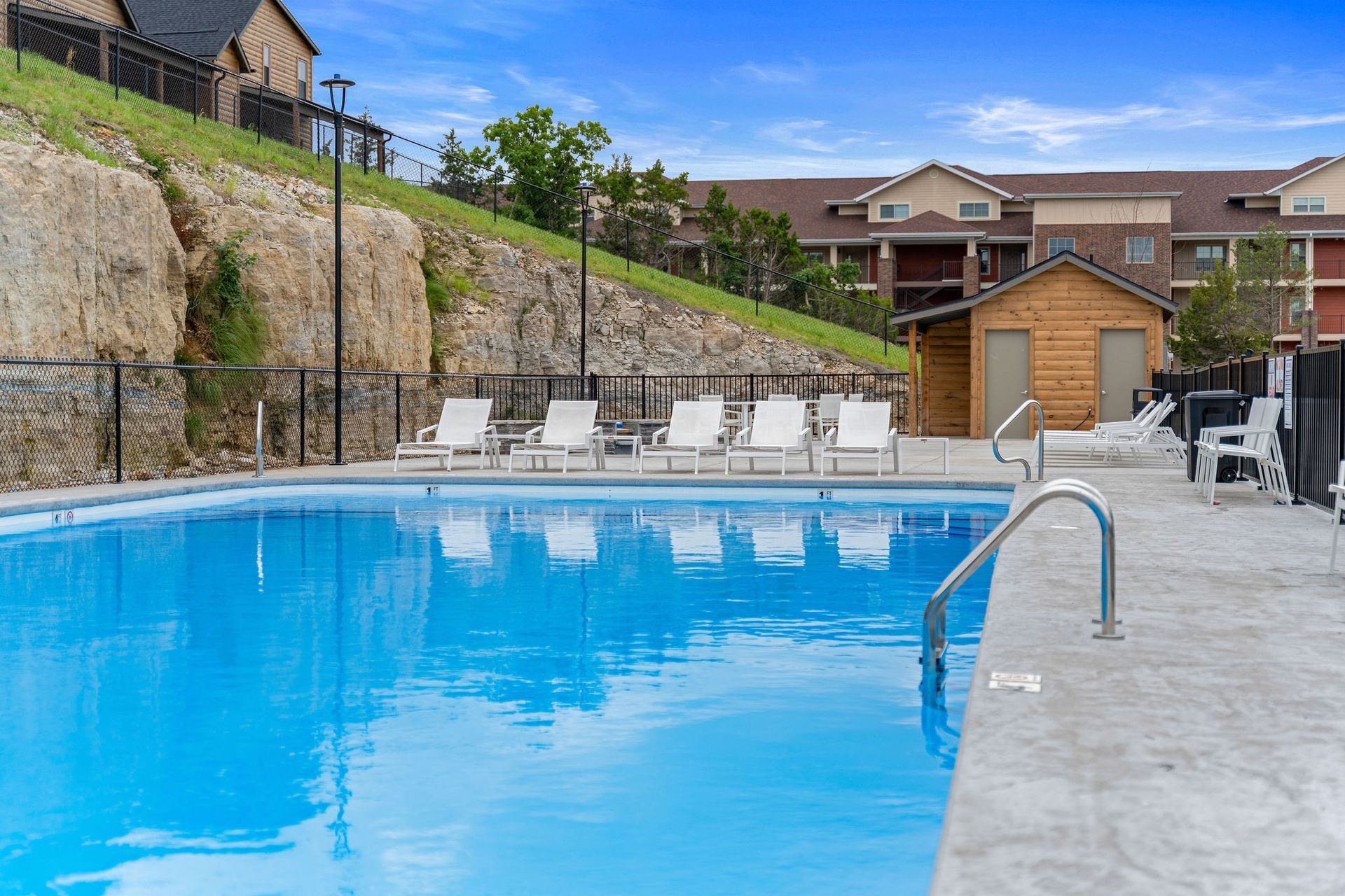 Outdoor swimming pool with blue water, lounge chairs, and a stone deck beside a hillside building