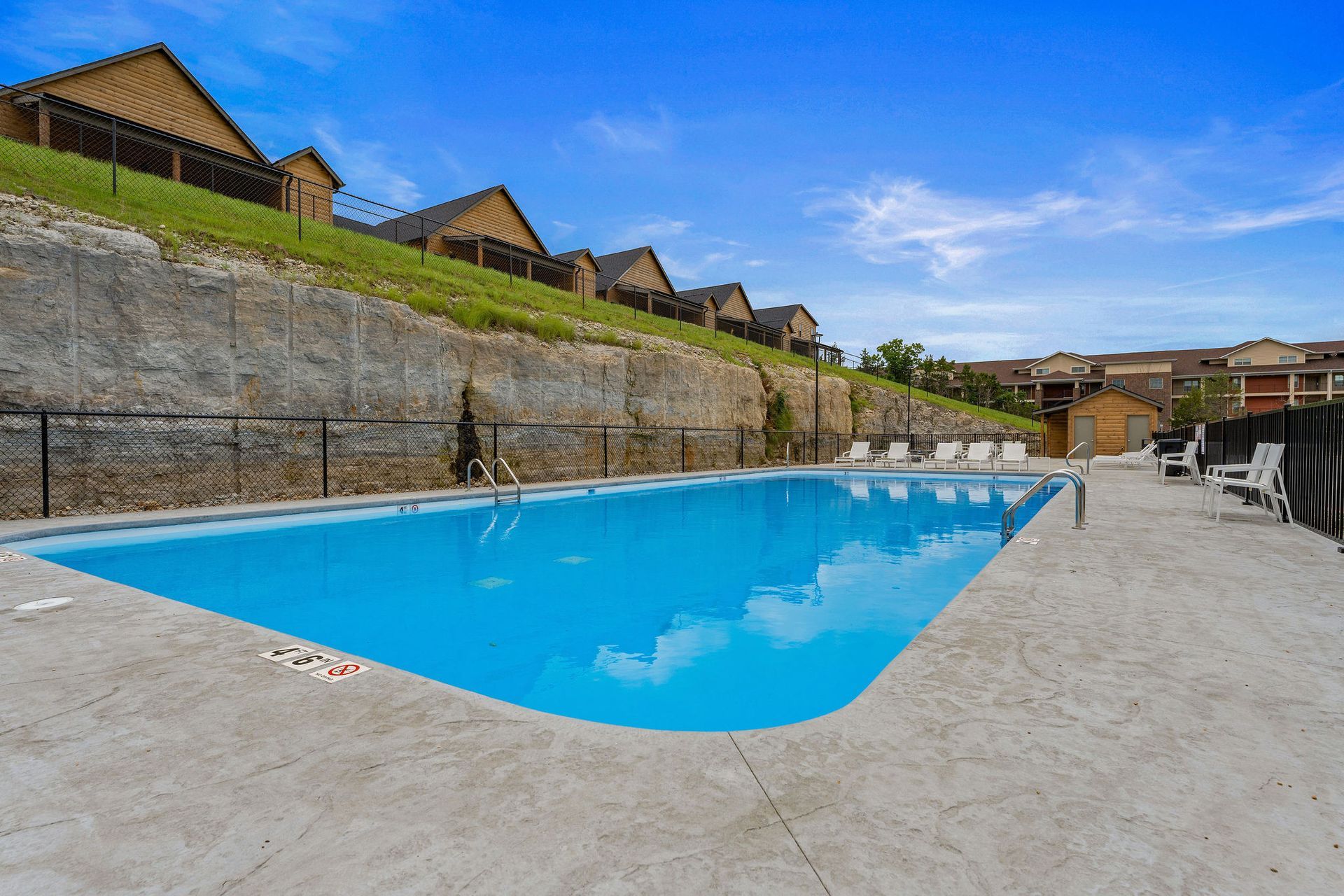Outdoor swimming pool with bright blue water beside a stone wall and lounge chairs under a clear sky