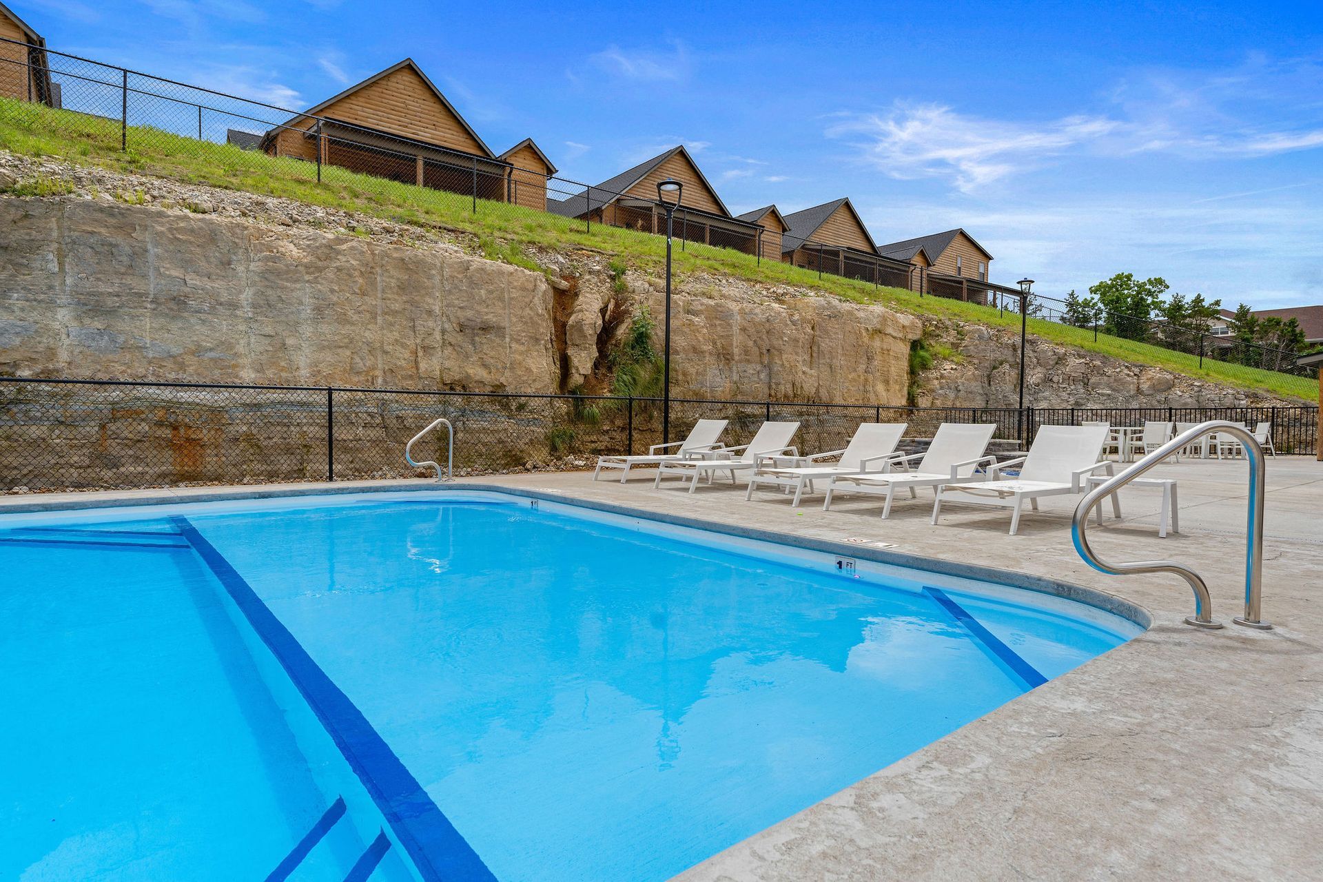 Outdoor swimming pool with blue water, lounge chairs, and stone retaining wall under a clear sky