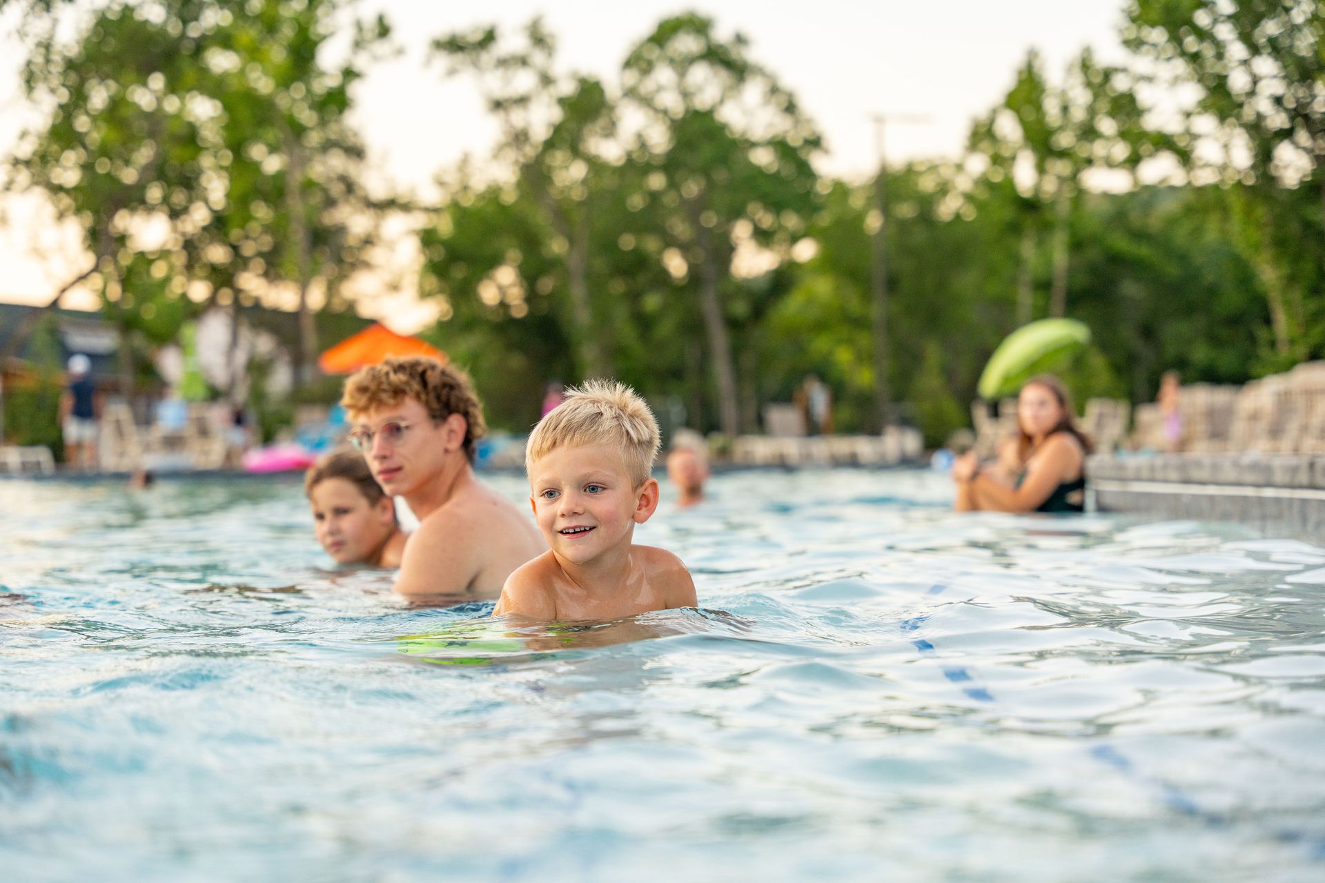 Children in a pool with adults, splashing in shallow water outdoors at a resort