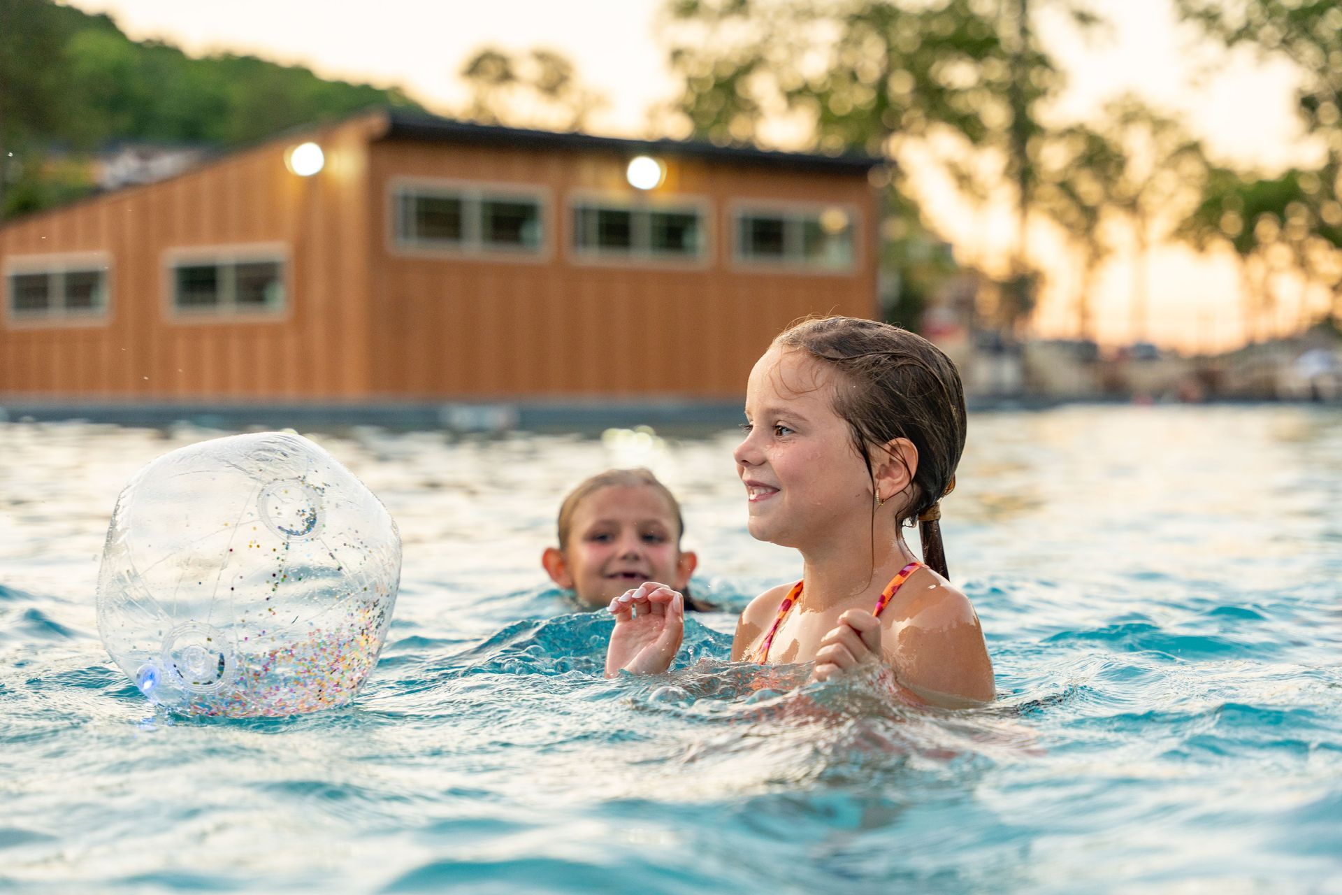 Children playing in a pool, splashing water near a building at sunset.