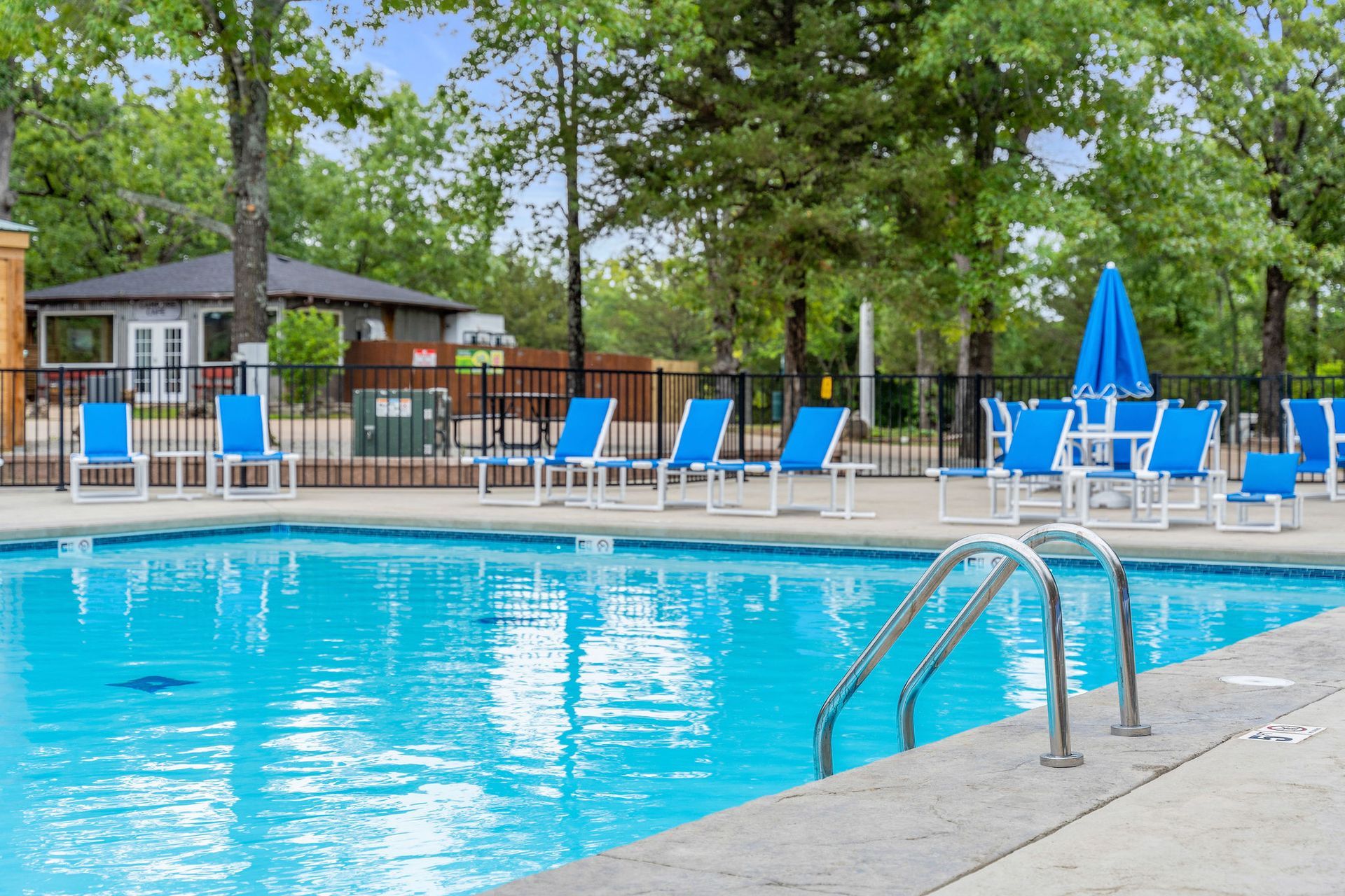 Outdoor swimming pool with blue lounge chairs, umbrellas, and surrounding trees
