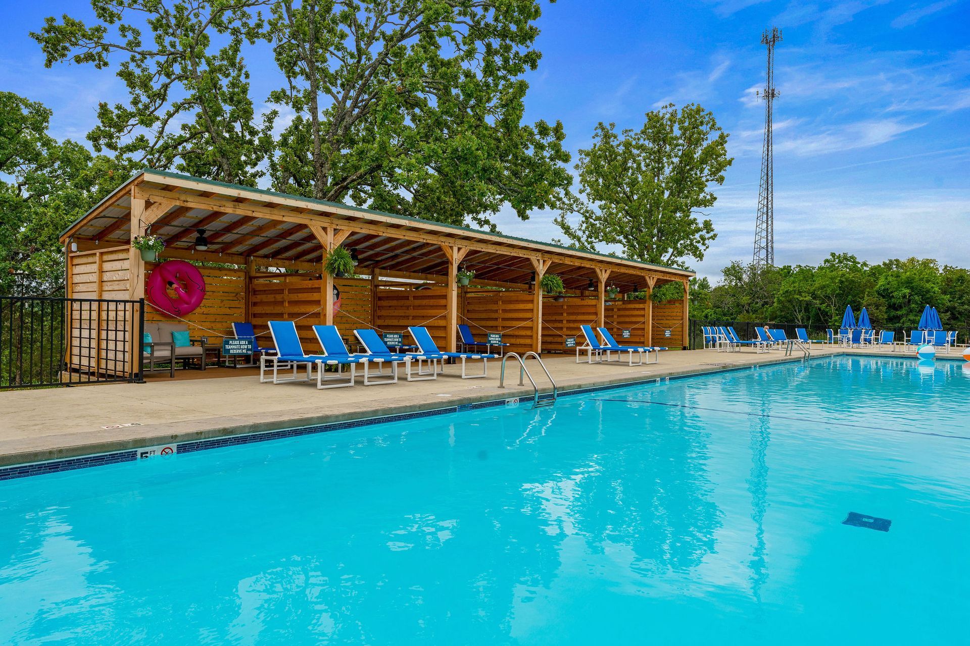 Outdoor resort pool with blue lounge chairs under a wooden cabana and trees nearby
